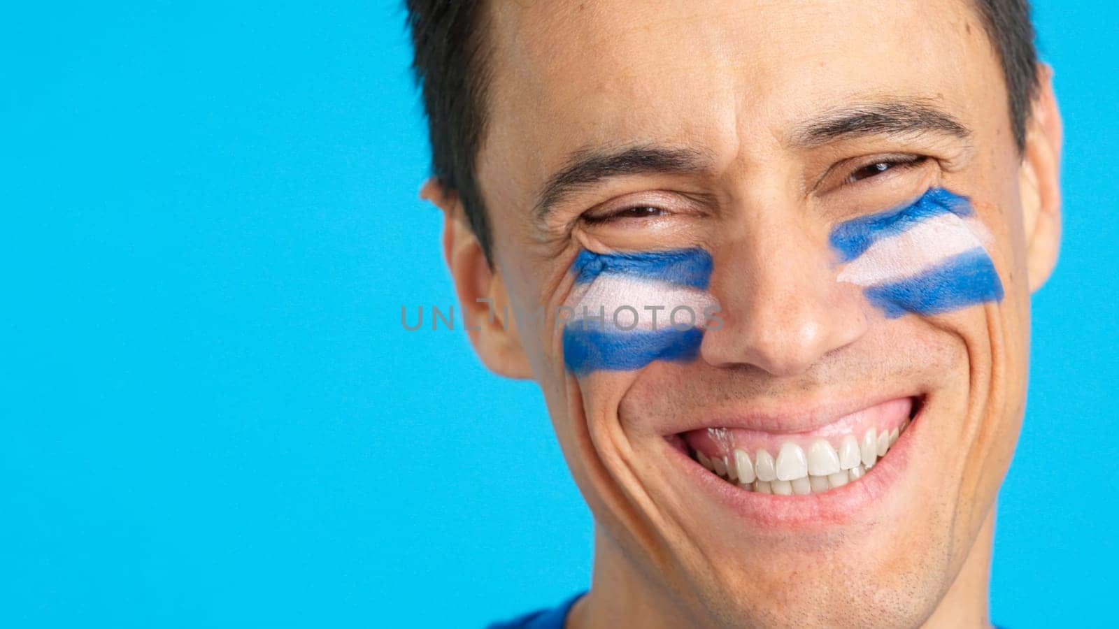Close up of a man with a salvadoran flag painted on the face smiling at camera