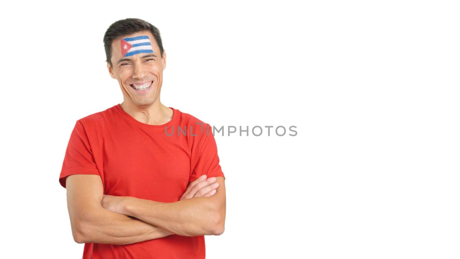 Man standing with cuban flag painted on face smiling with arms crossed