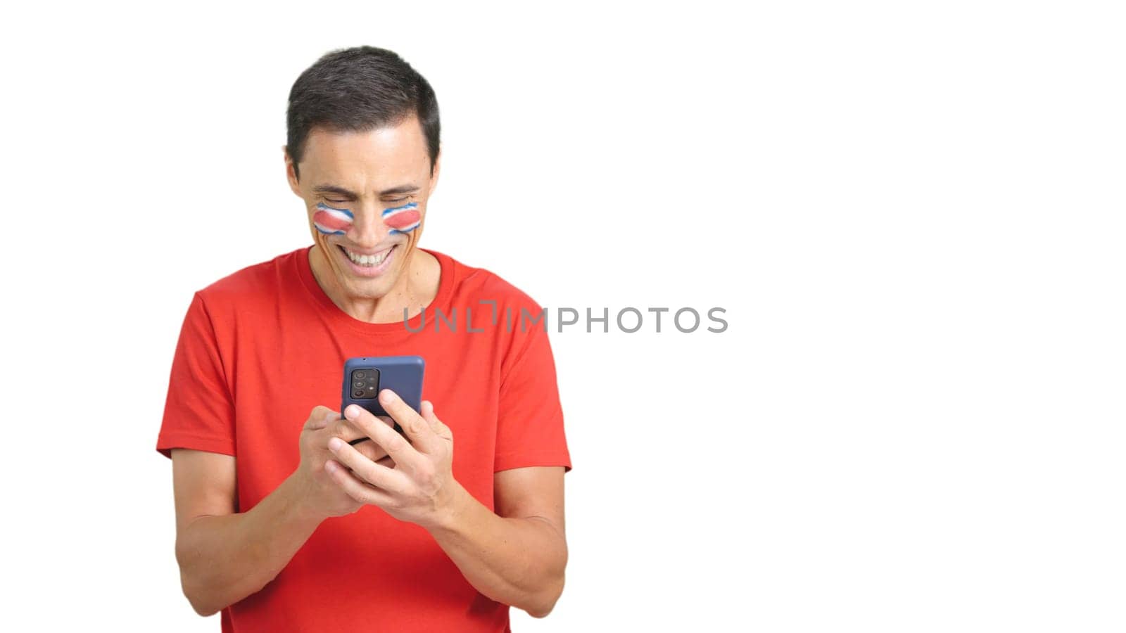 Costa rican supporter with the flag of Costa Rica painted on his face, looking at his mobile phone smiling