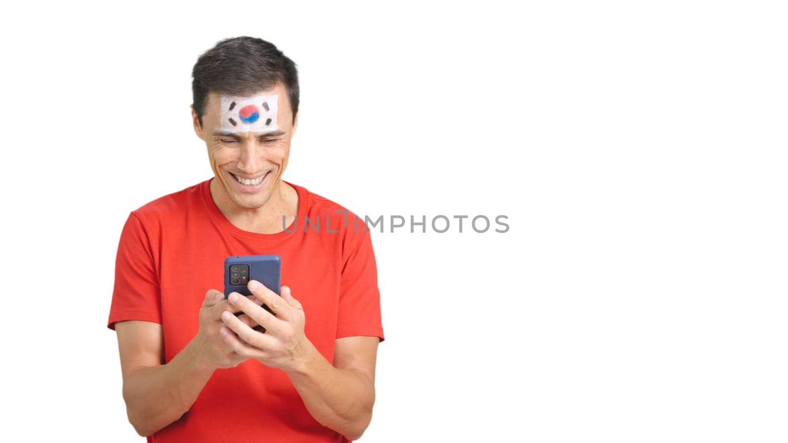 South Korea supporter with the flag of South Korea painted on his face, looking at his mobile phone smiling