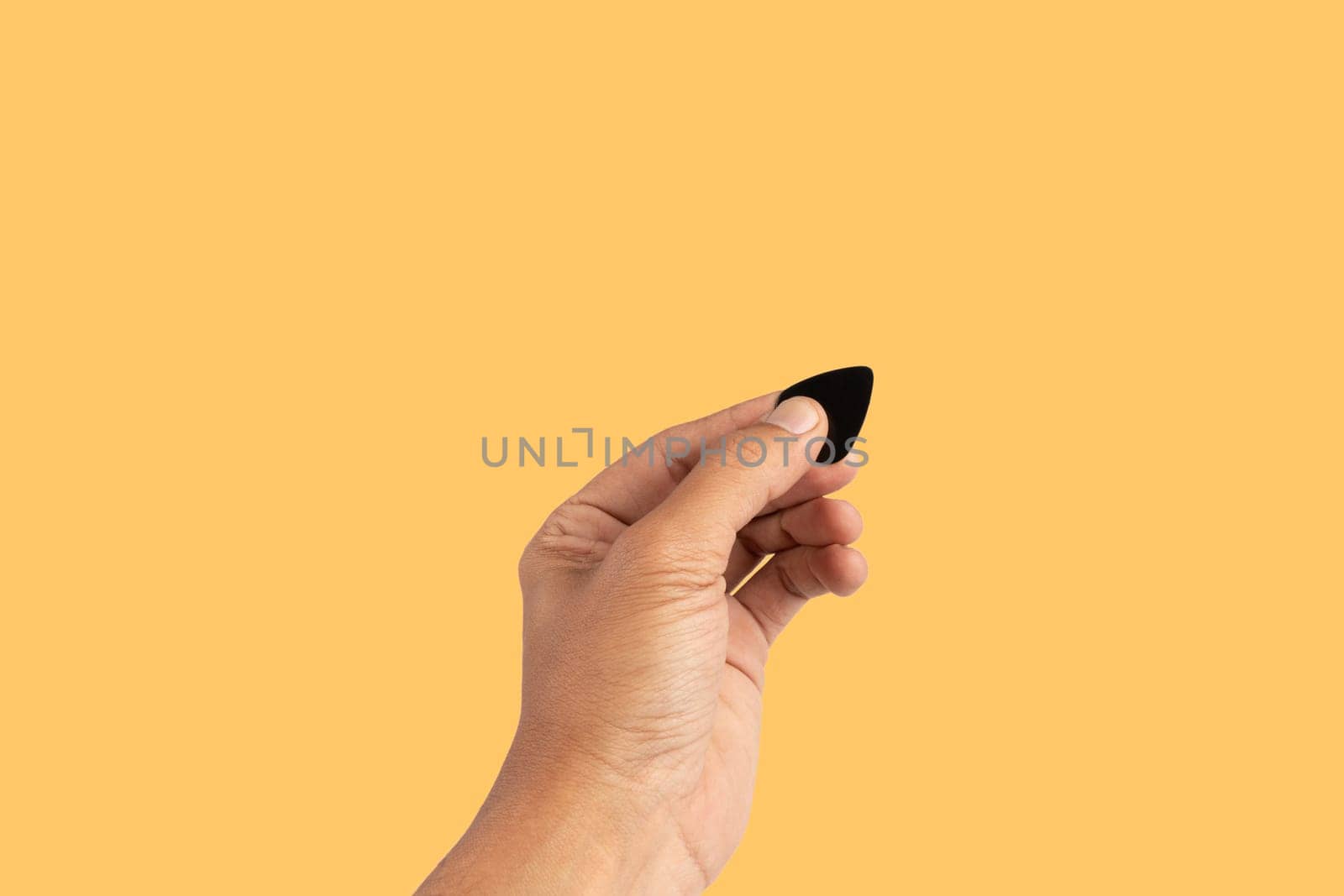 Black male hand holding a guitar pick isolated on yellow background by TropicalNinjaStudio