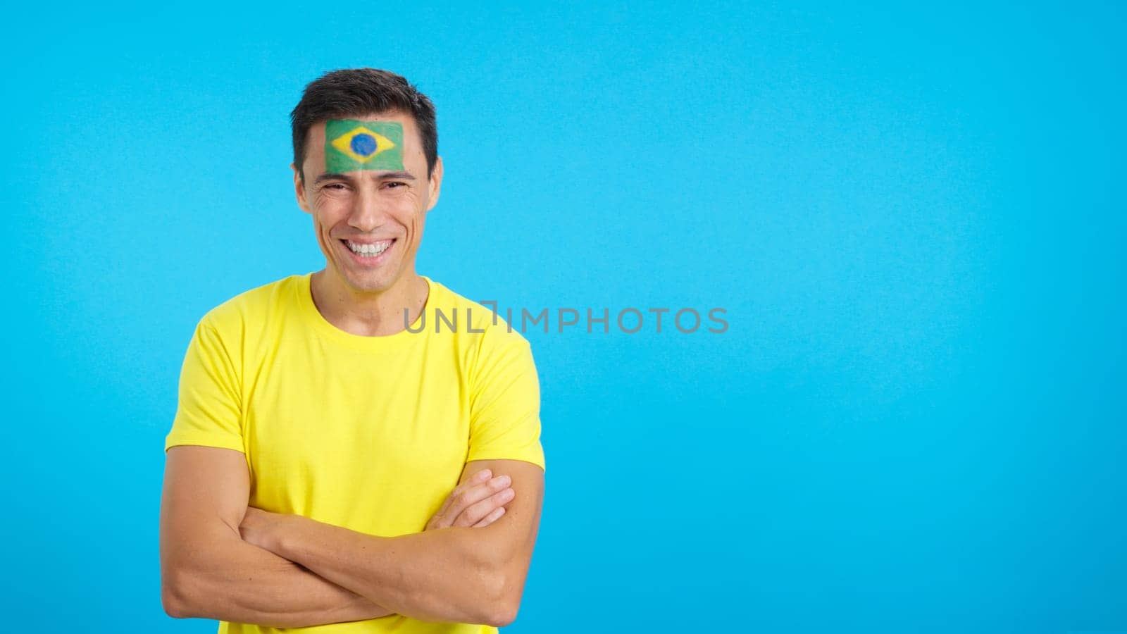 Man standing with brazilian flag painted on face smiling with arms crossed