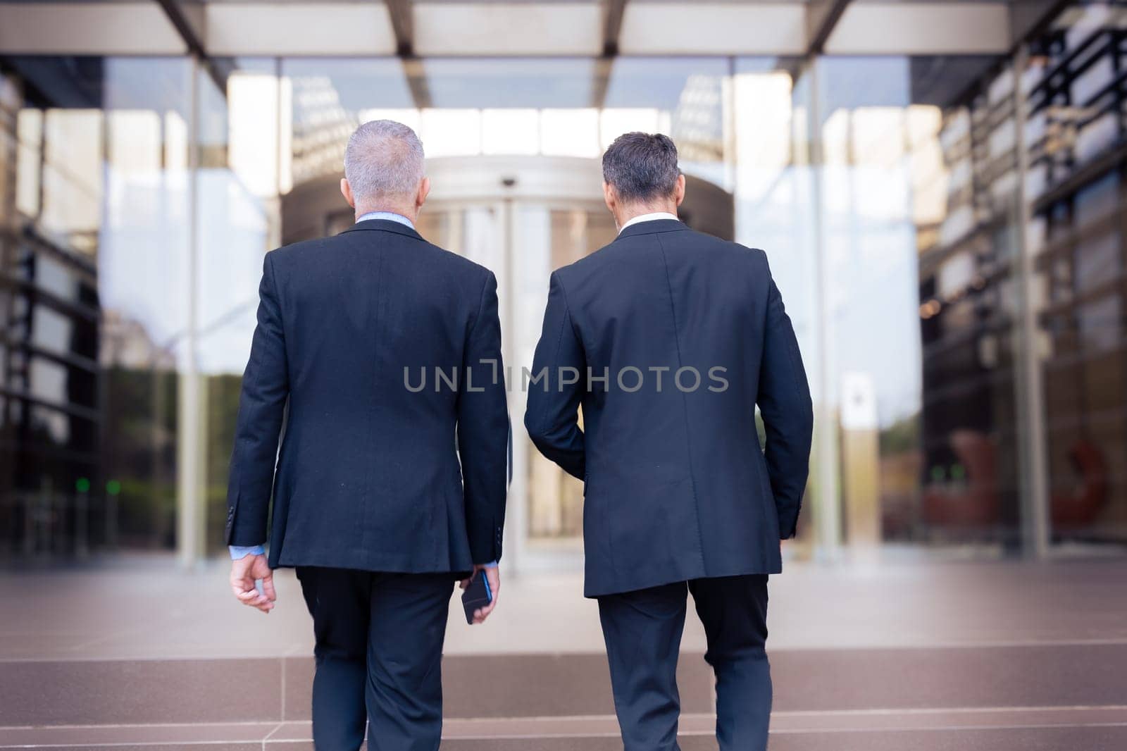 two caucasian male business colleagues talking happily, co-workers talking walking to enter the office building where they work