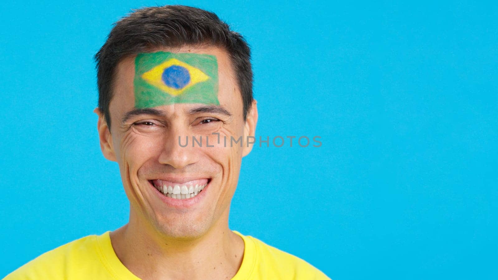 Close-up of a caucasian man with a brazilian flag painted on the face smiling at camera
