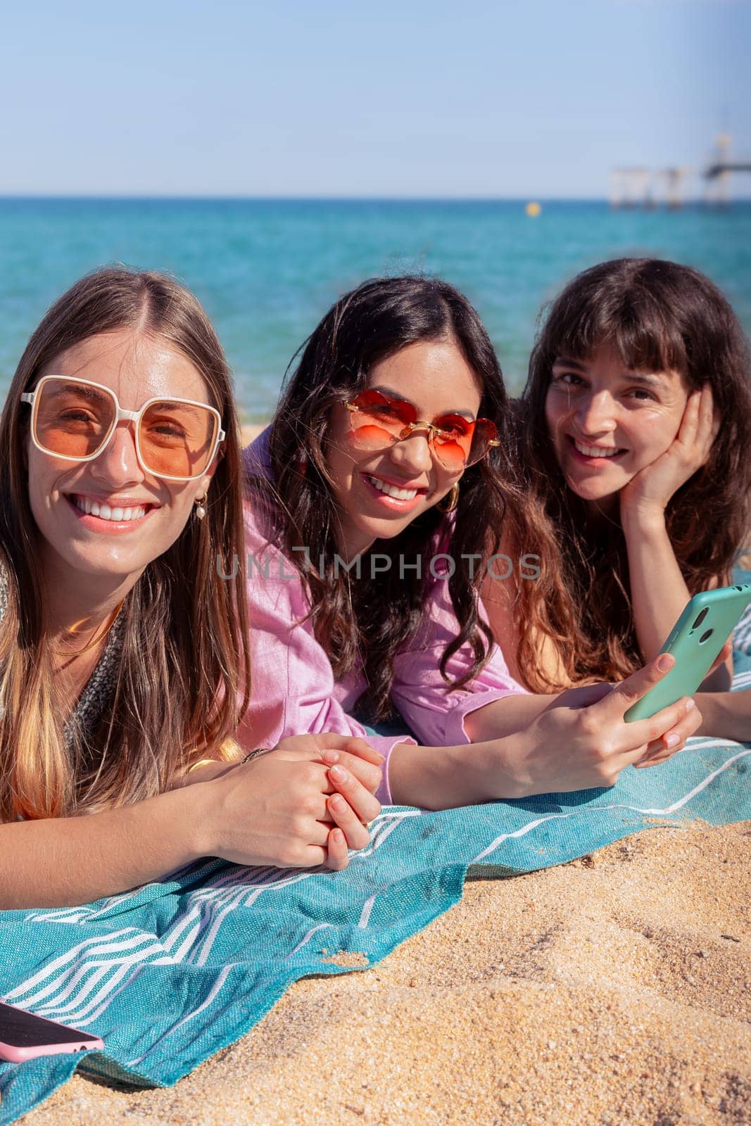 Group of smiling multiethnic women enjoying vacation. Beautiful and cheerful Gen Z girls with their mobile phones pose looking at the camera with a mobile phone.