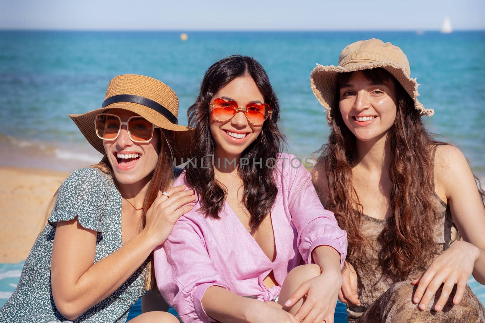 Group of smiling multiethnic women wearing hats and sunglasses enjoying vacation. Beautiful and cheerful Gen Z girls pose looking at the camera