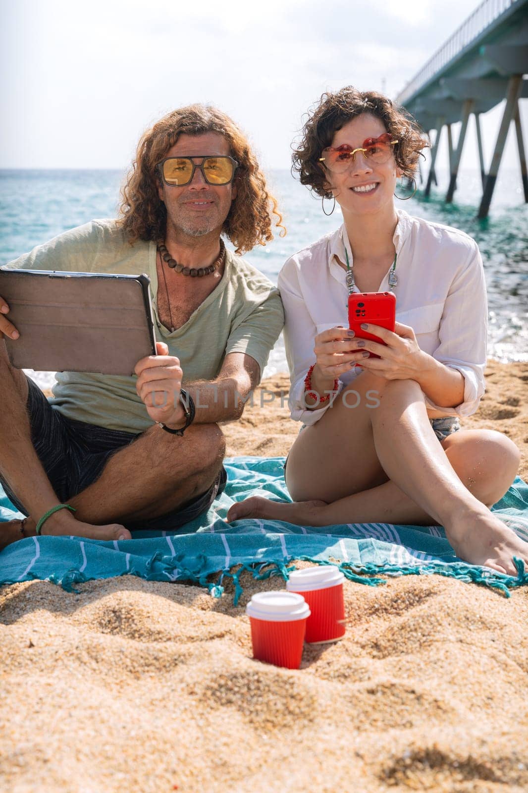 Vertical portrait smiling couple on the beach browsing smartphone apps. by mariaphoto3