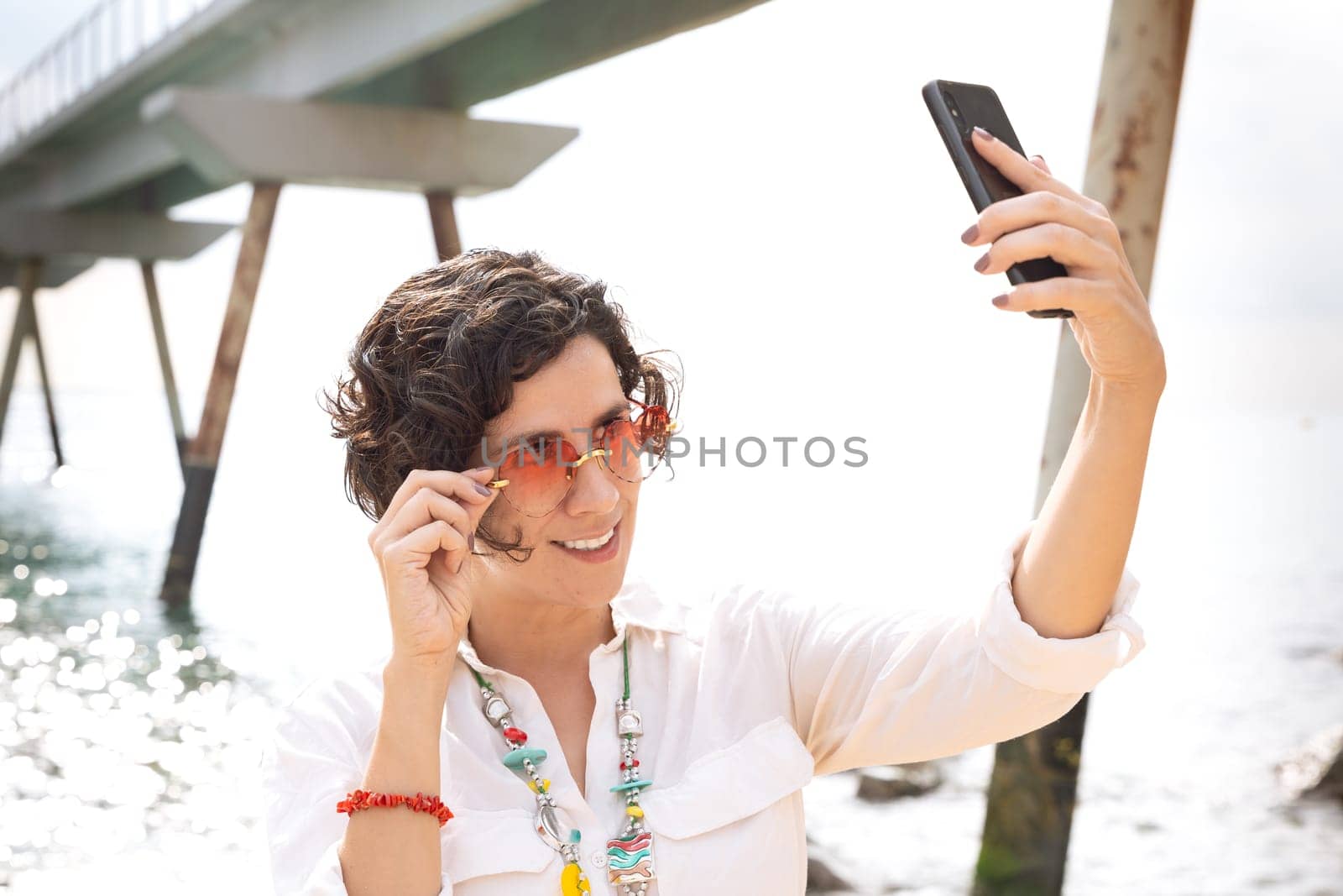 Front view of a caucasian woman wearing sunglasses on vacation by the sea laughing greeting by video call to a family member