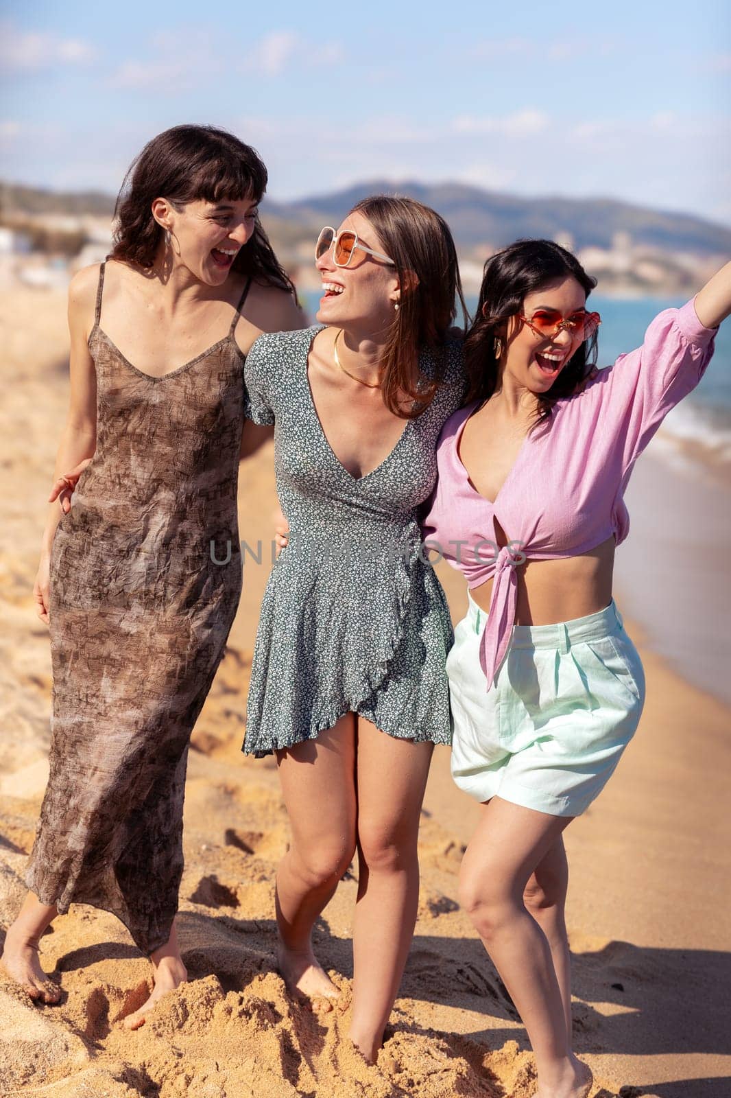 Vertical portrait of three female friends walking on the beach having fun. by molesjuny