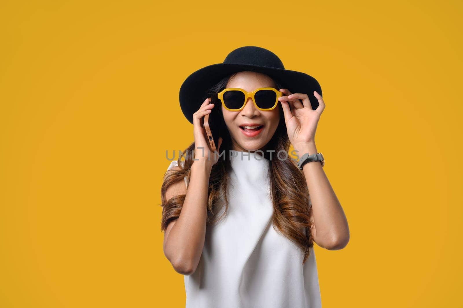 Smiling young woman wearing summer clothing talking on mobile phone isolated on yellow background.