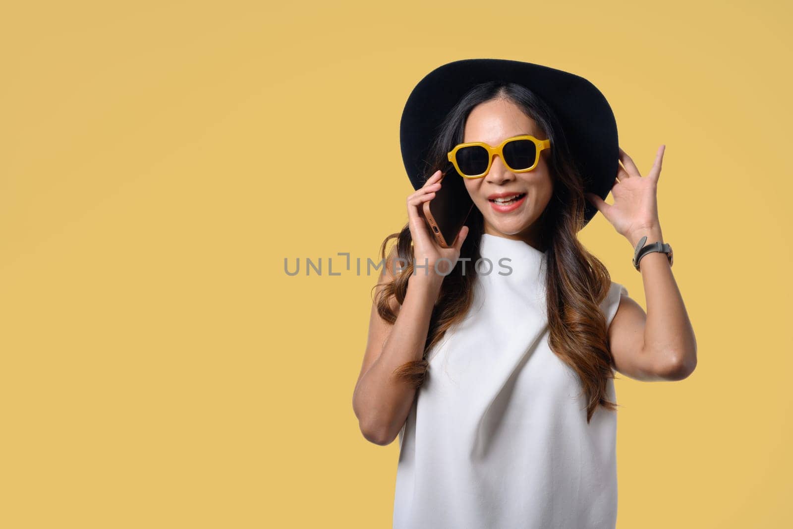 Smiling young woman wearing summer clothing talking on mobile phone isolated on yellow background.