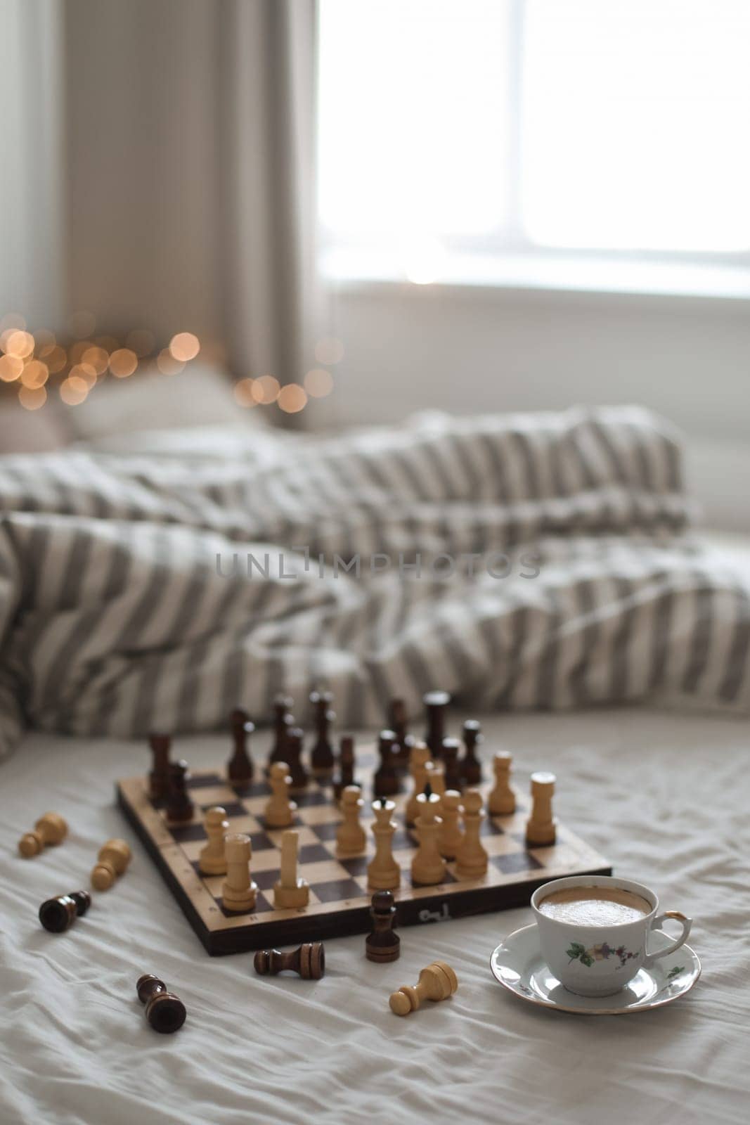 Chess board with cup of coffee on bed. Strategy thinking. Morning ideas concept. Pastel shades. High quality photo. Top view of unmade bedding sheets and pillow.