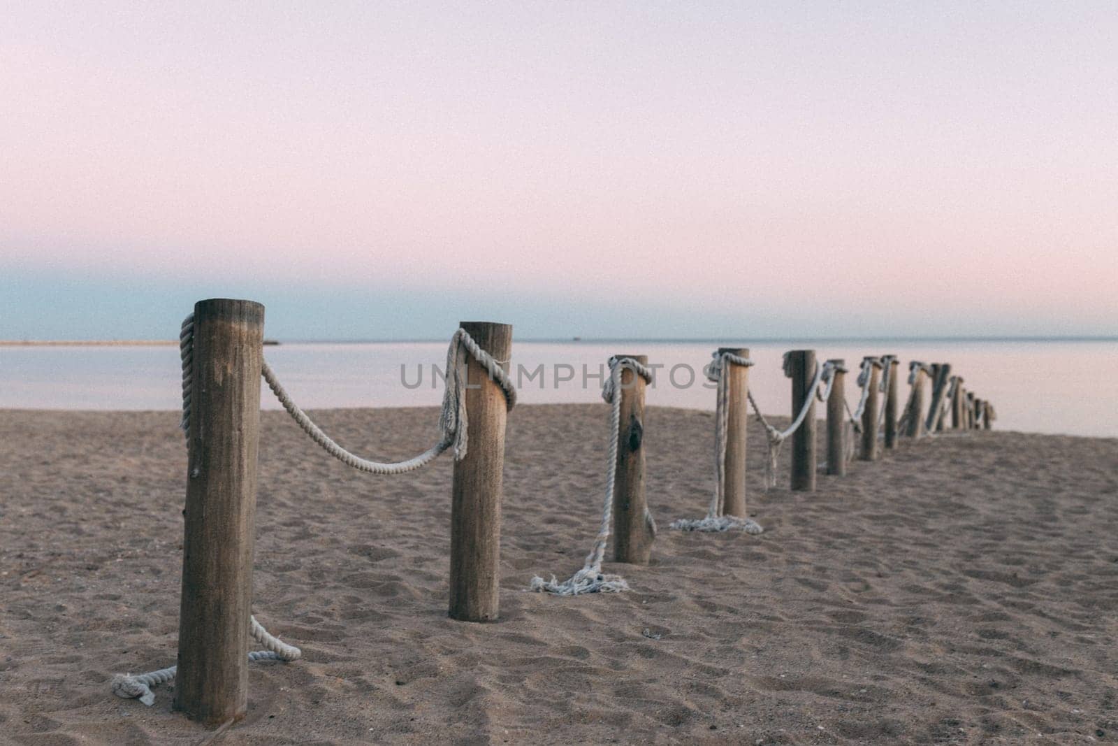 A row of wooden posts with rope tied to them on a beach. The beach is calm and peaceful, with the ocean in the background