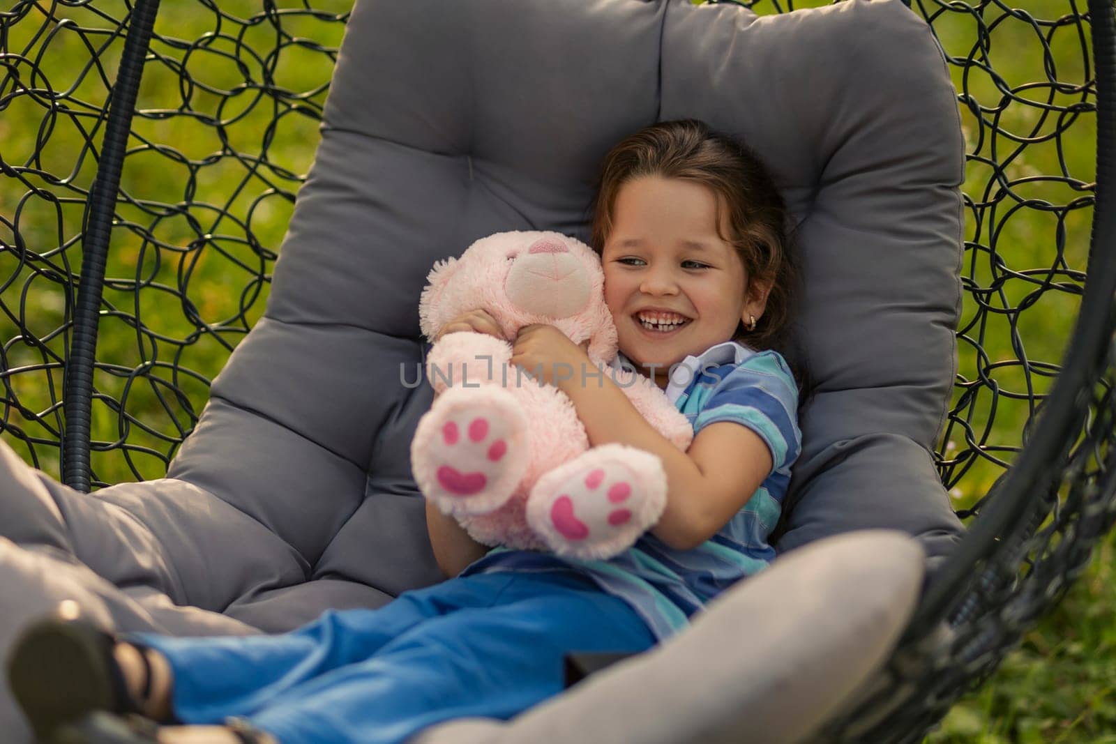 child hugging a teddy bear while sitting in a hanging chair