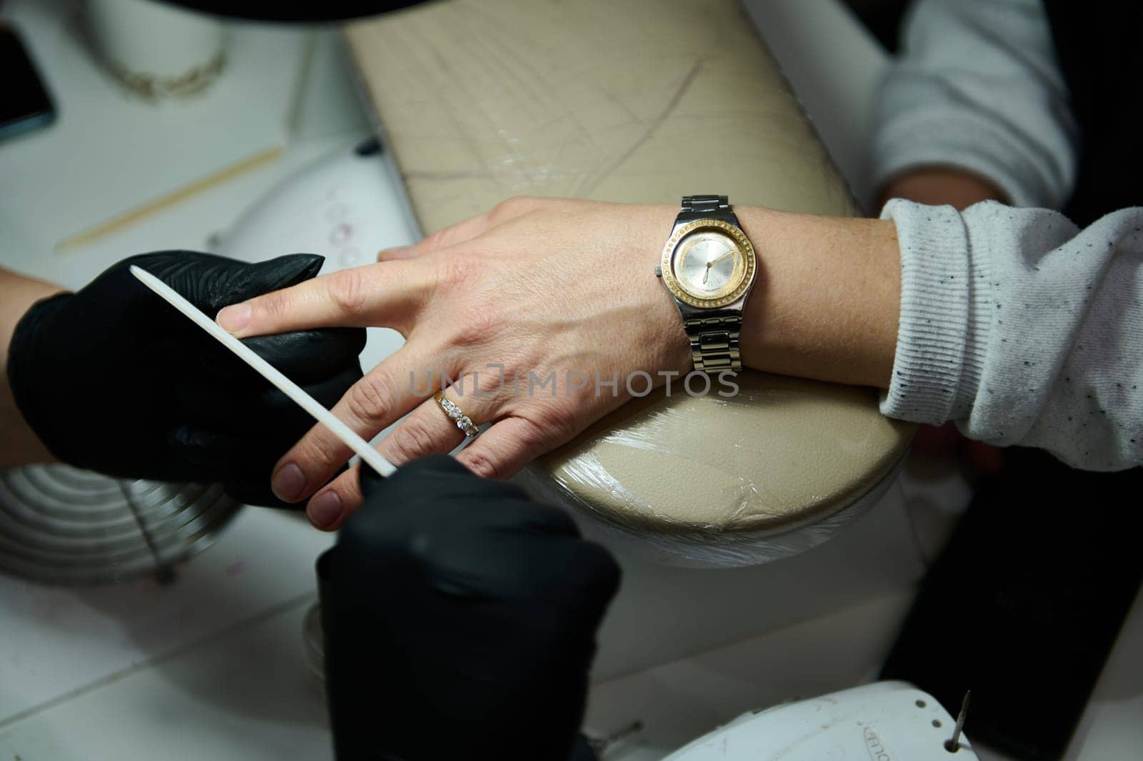 Close-up of a professional manicure session at a beauty salon. A nail technician carefully files a client's nails, providing detailed nail care and attention.