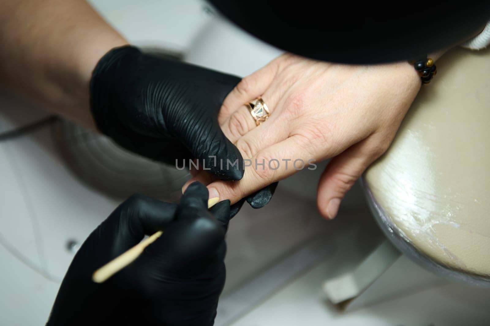 A close-up shot of a nail technician wearing gloves, providing a manicure to a client in a beauty salon. Professional nail care and hygiene.