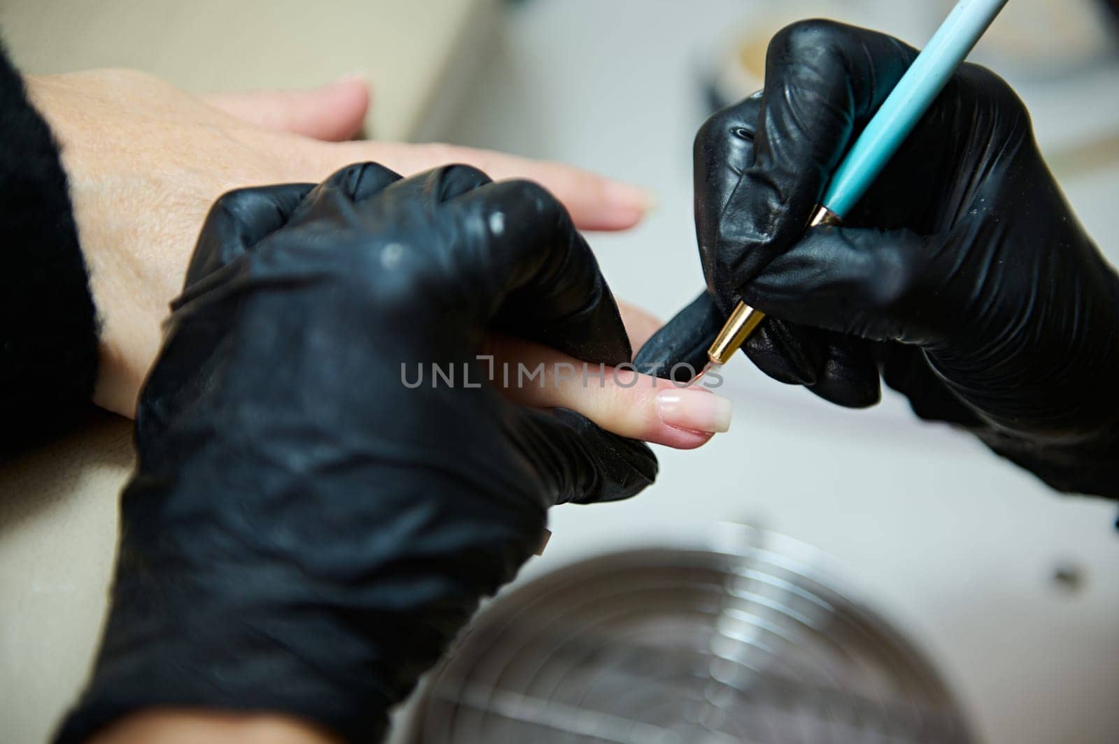 Close-up of a professional manicure treatment at a beauty salon. The technician is wearing black gloves and using tools to shape the client's nails.