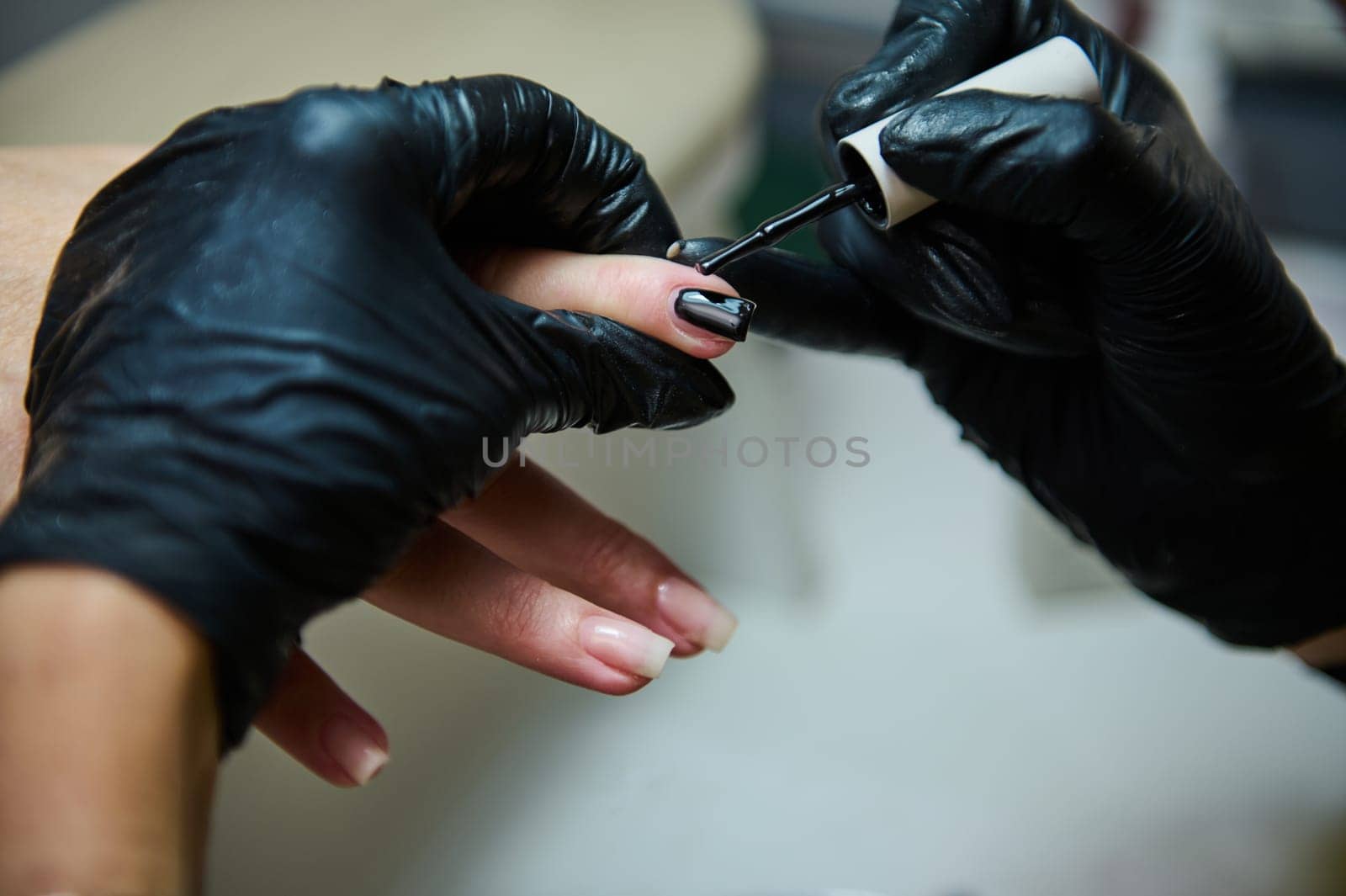 Close-up of a professional manicure treatment in a beauty salon. A nail technician is applying black nail polish.