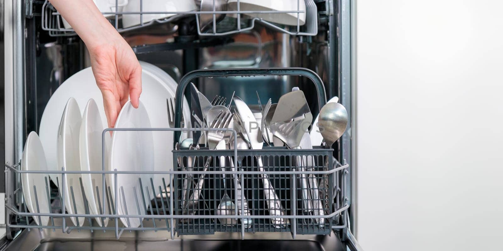 Female hand unloading dishwasher with tableware. Kitchen appliances, lifestyle view. Woman takes a plate from the dishwasher. Concept of modern technologies in the kitchen