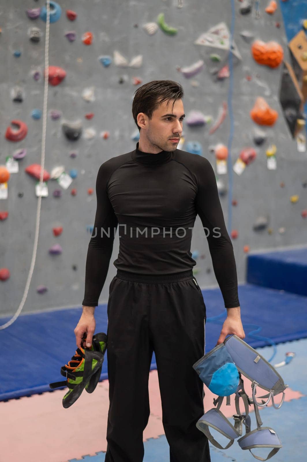 Portrait of a Caucasian man with a climbing harness in his hands in a climbing wall