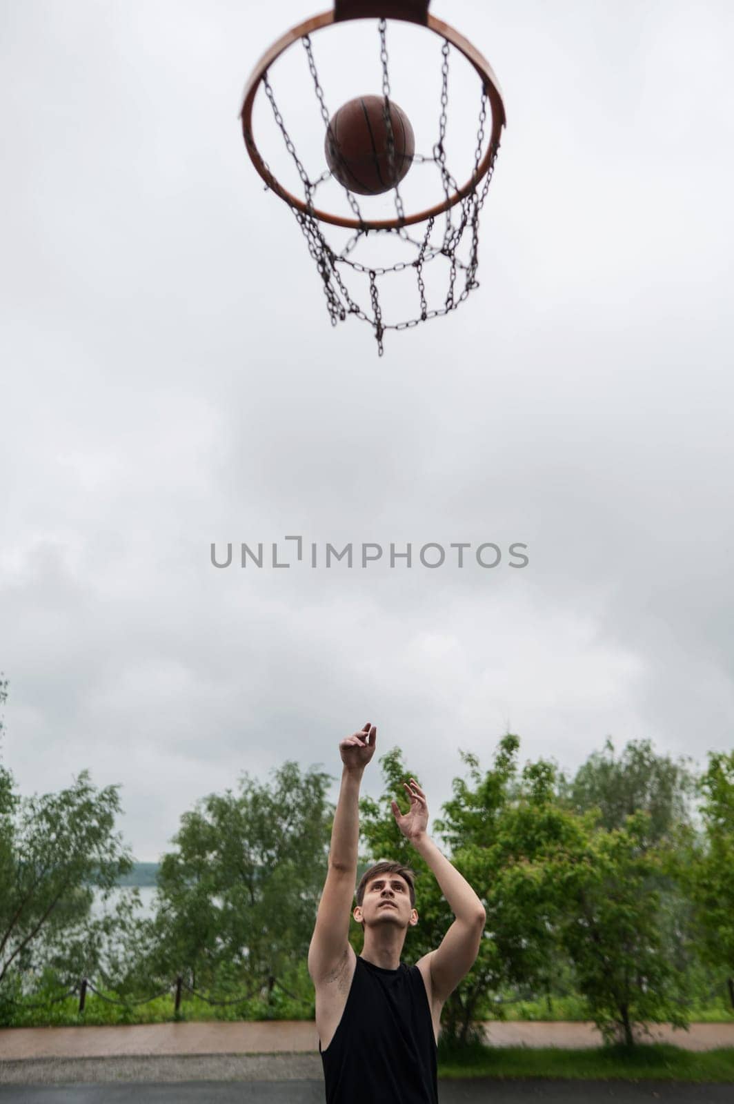 A Caucasian man shoots a ball into a basketball basket outdoors. Vertical photo. by mrwed54