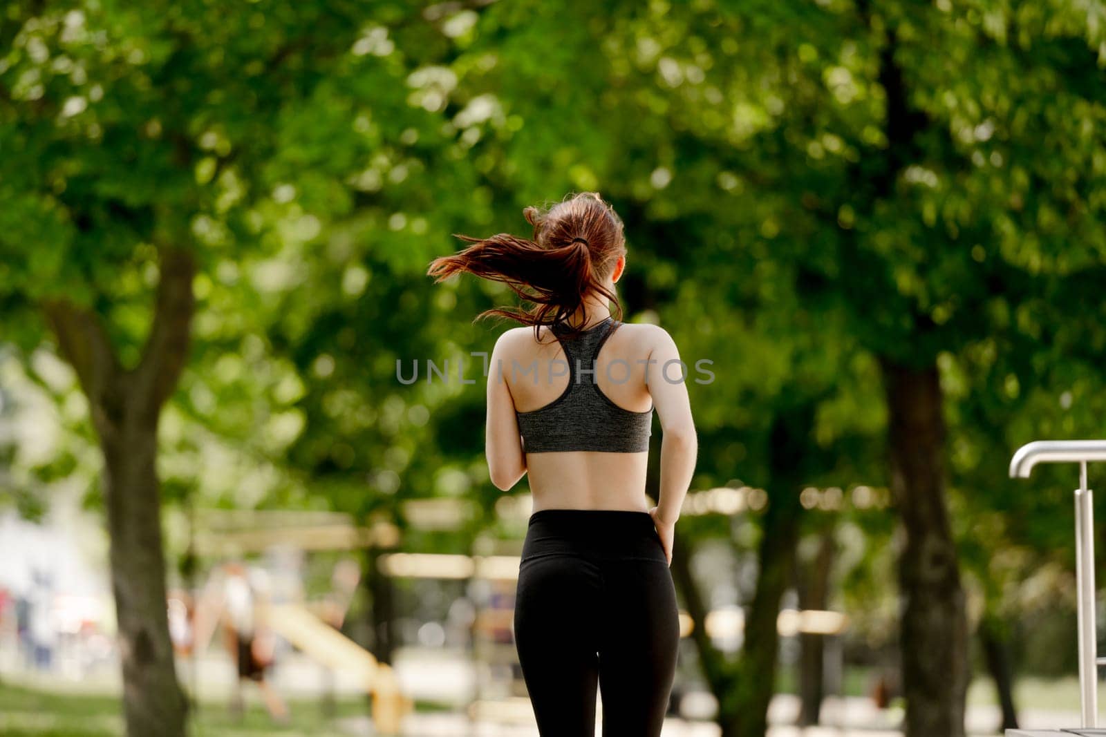 Young Girl Enjoys Morning Run In Park, View From Behind