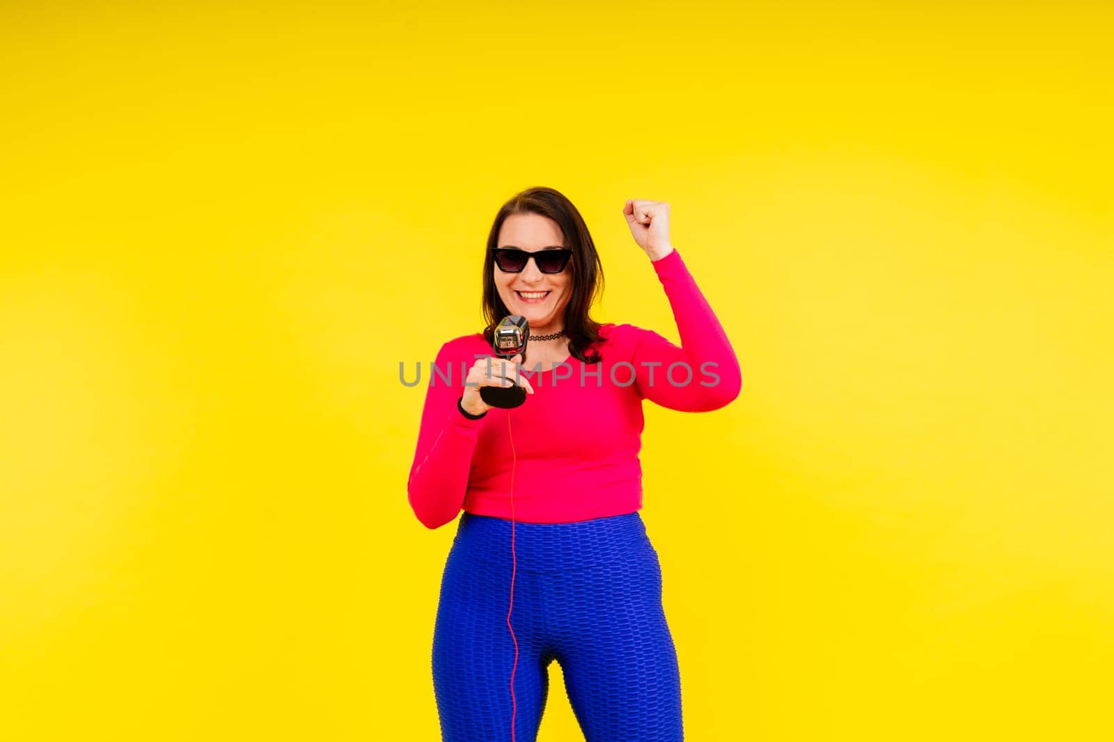 Smiling brunette woman with microphone on colored studio background by Zelenin