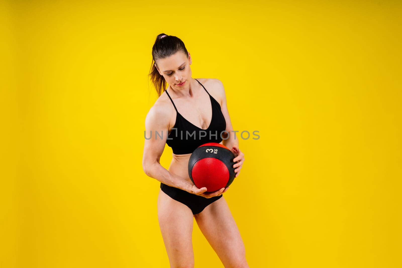 Portrait of a fitness happy fit woman standing holding a medicine ball. Copy Free space for text. Slim caucasian cross fit woman with fitness ball stand in gym, look. Plain light wall background