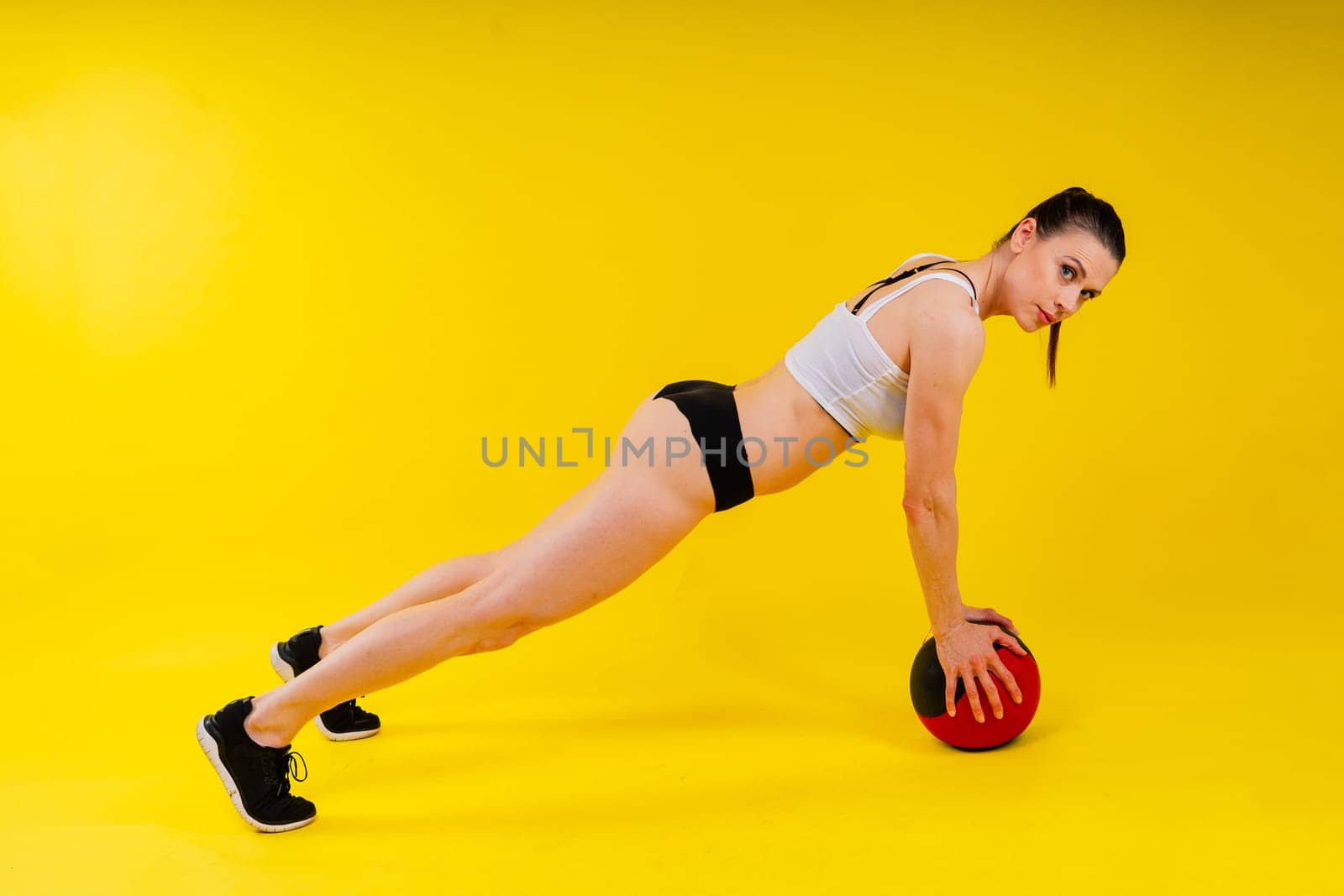 Portrait of a fitness happy fit woman standing holding a medicine ball. Copy Free space for text. Slim caucasian cross fit woman with fitness ball stand in gym, look. Plain light wall background