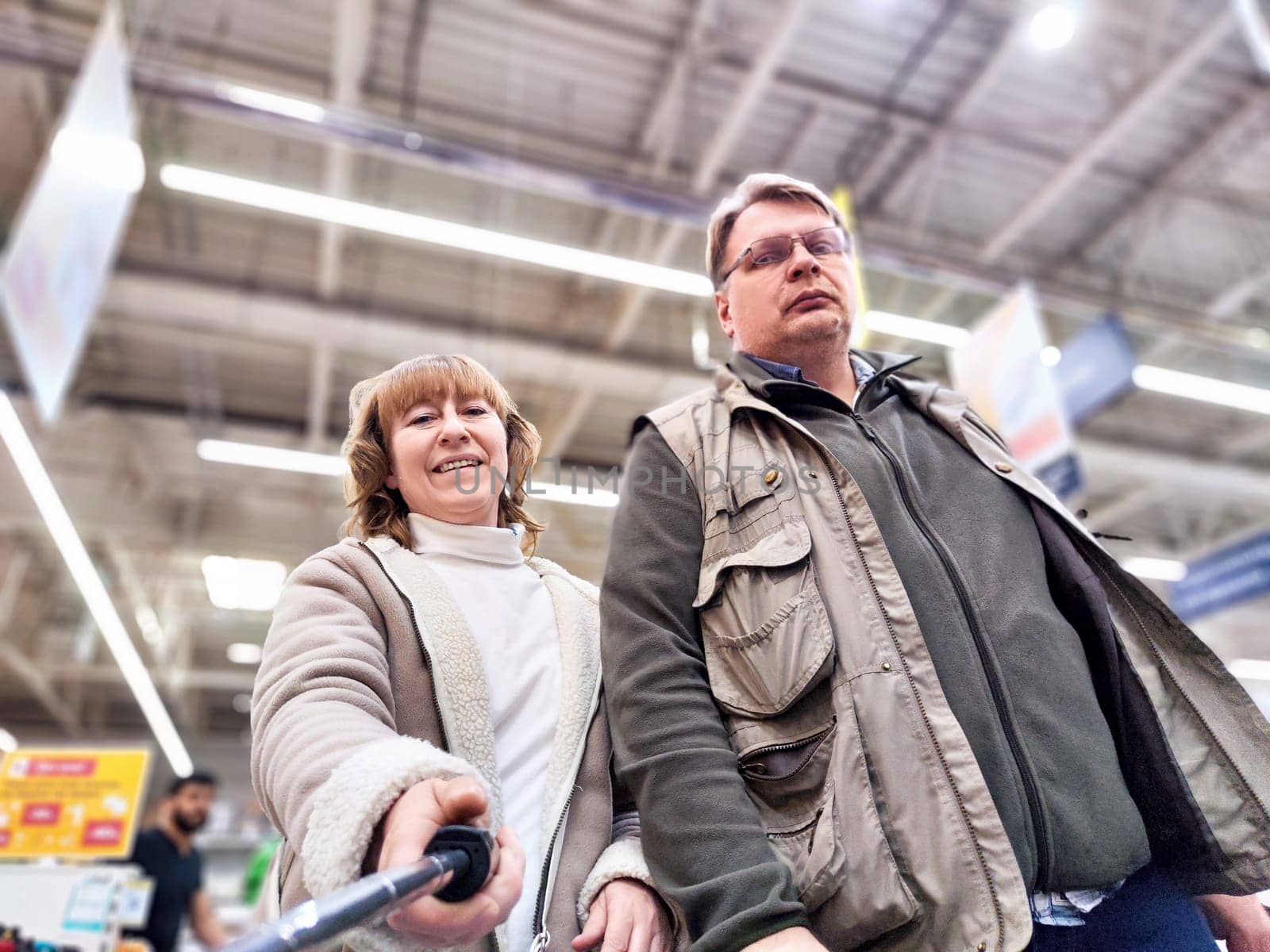 A middle-aged couple is shopping in brightly lit retail store, looking around with interest