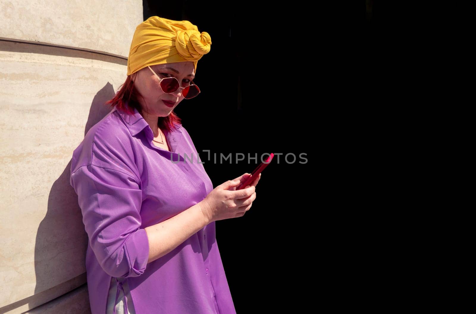 Happy and funny cool lady with fashionable clothes on dark background look to the phone seriously and thoughtfully - adult asian with extravagant style isolated on black background