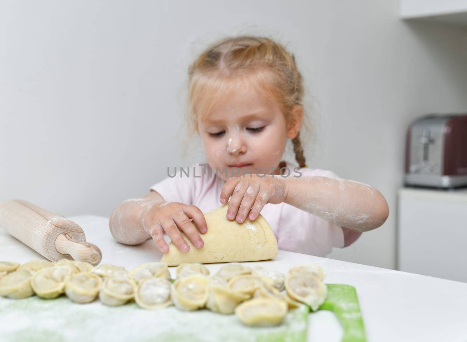 Little girl in flour prepares dumplings in the kitchen
