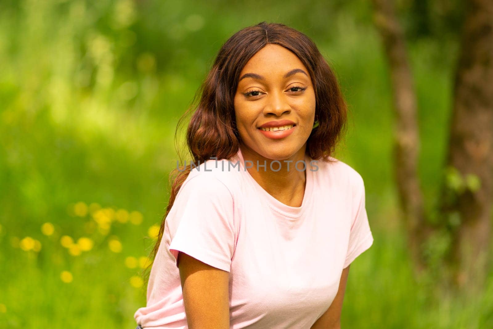 young black woman sitting on a bench in a park on a summer afternoon. by Ceballos