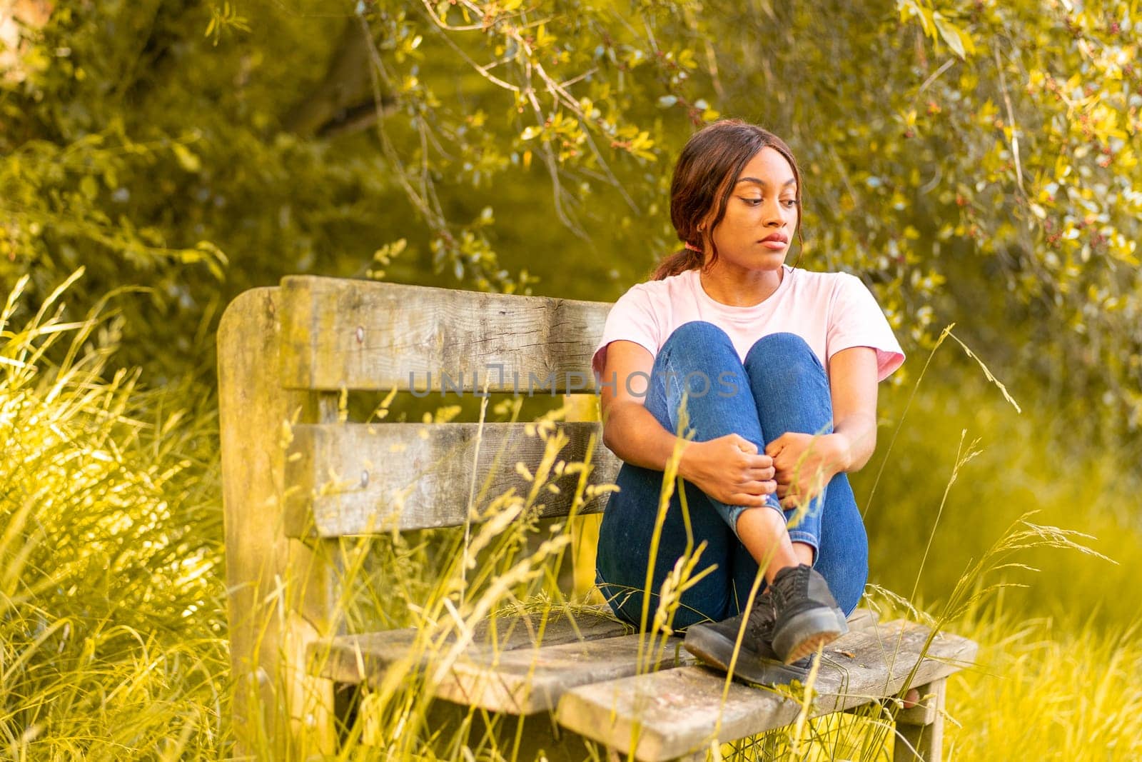 young black woman sitting on a bench in a park on a summer afternoon. by Ceballos