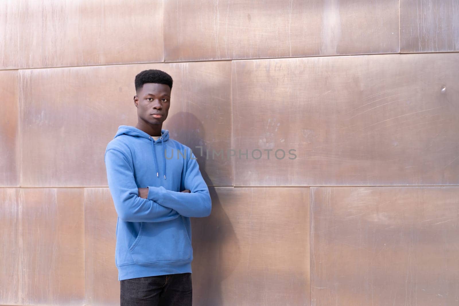 A young man in a blue hoodie stands in front of a wall by Ceballos