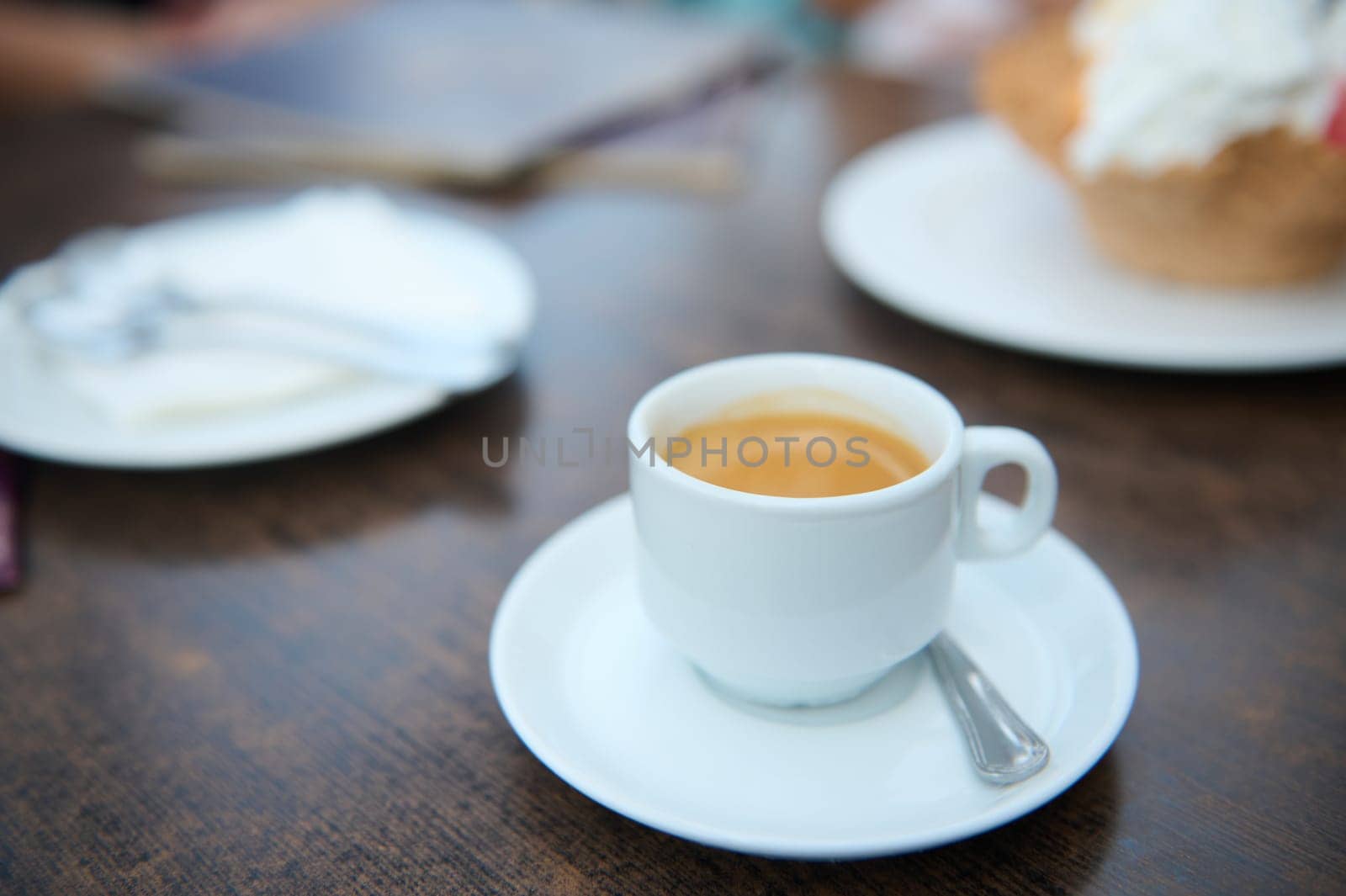 A close-up shot of a white coffee cup on a wooden table in a cafe. The image portrays a calm and relaxing atmosphere.