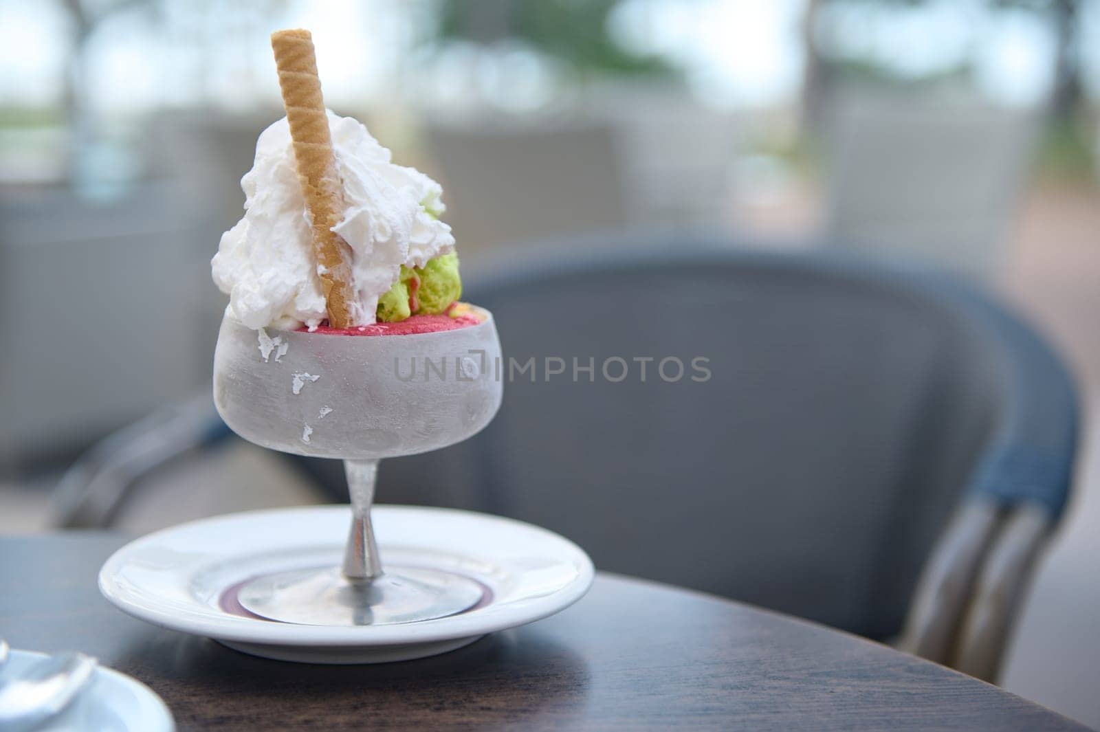 Close-up of delicious ice cream with whipped cream and waffle stick served in a frosted glass on a table in an outdoor cafe.