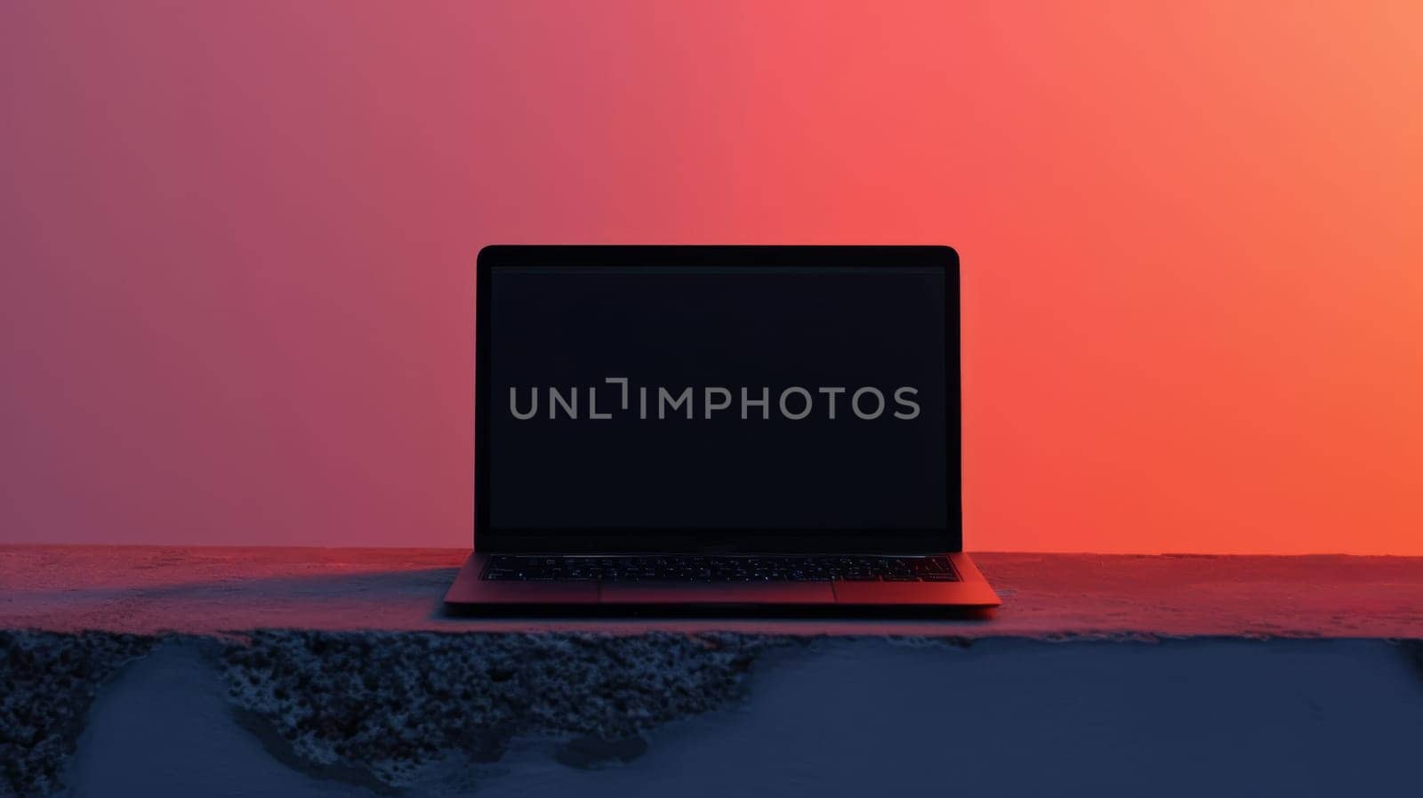 Laptop with blank screen on concrete ledge at sunset, minimalist technology concept.