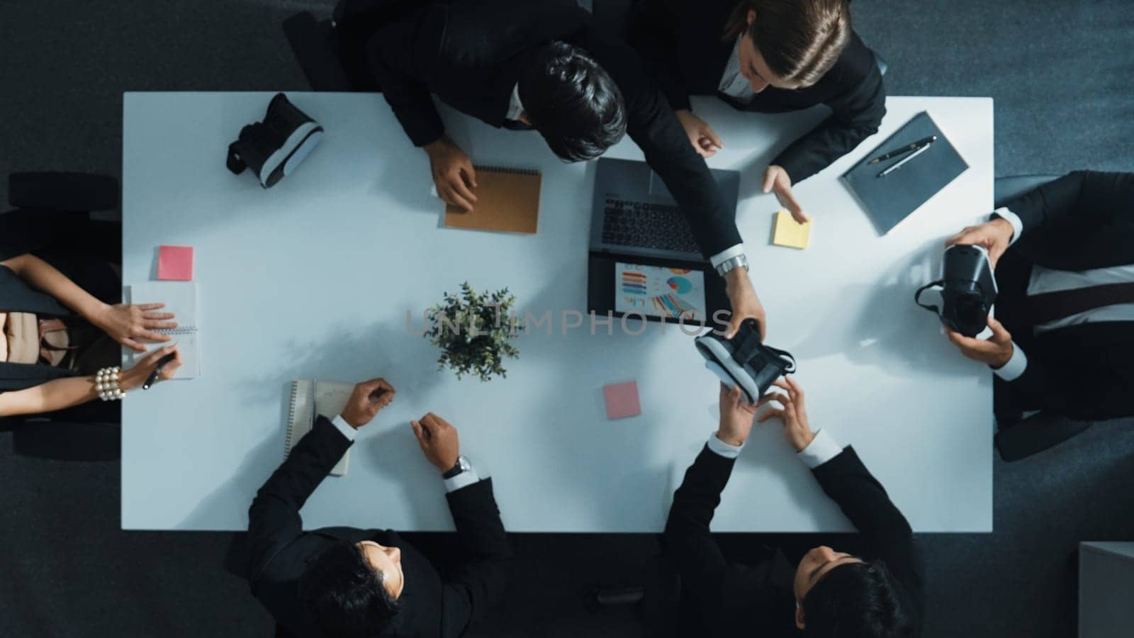 Top view of smart manager give vr head set to businesspeople while businesswoman prepare data analysis or analytic graph in laptop at meeting. Startup team preparing to enter meta verse. Directorate.