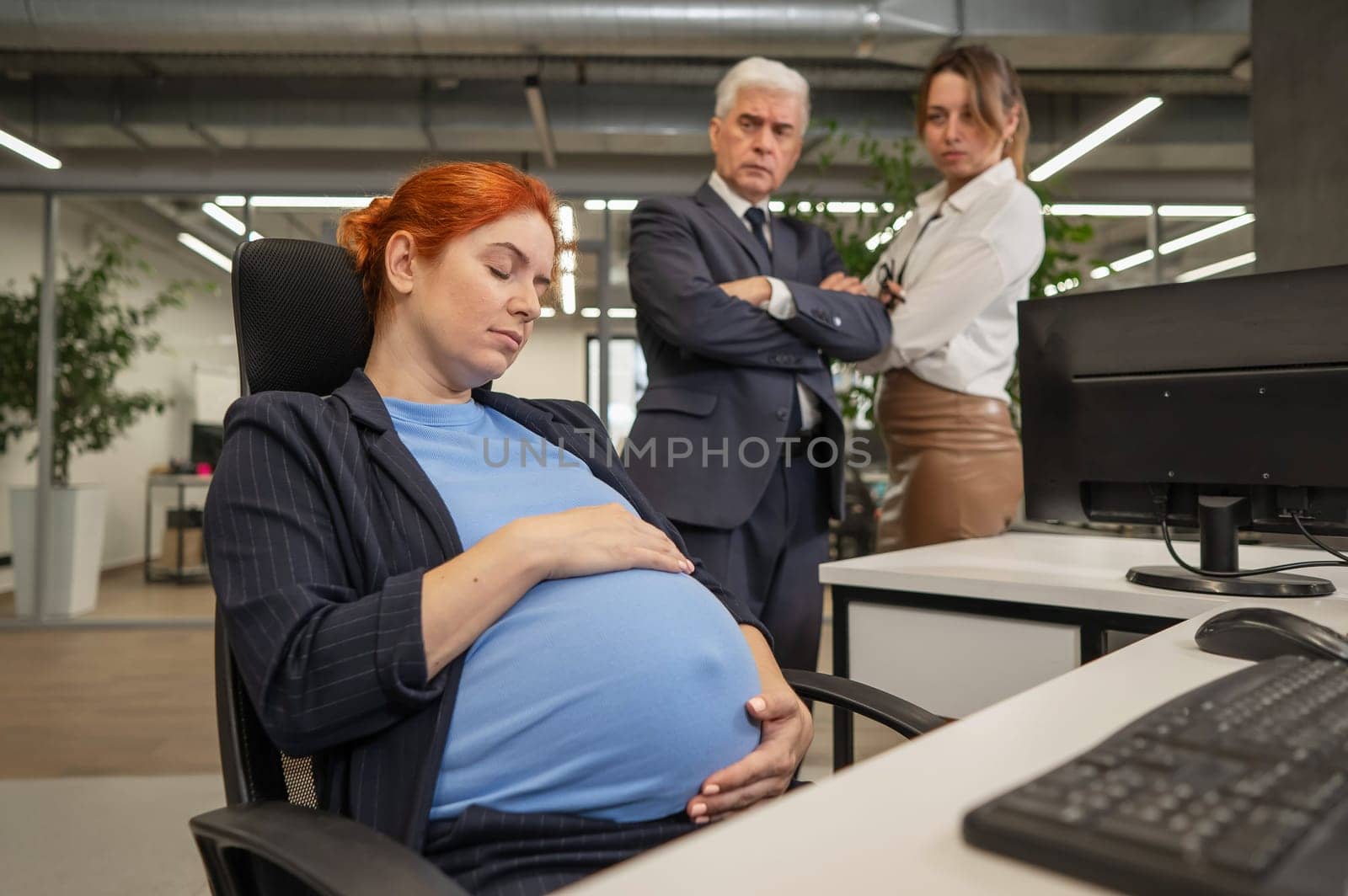 A pregnant woman sleeps at her workplace. Colleagues look disapprovingly. by mrwed54