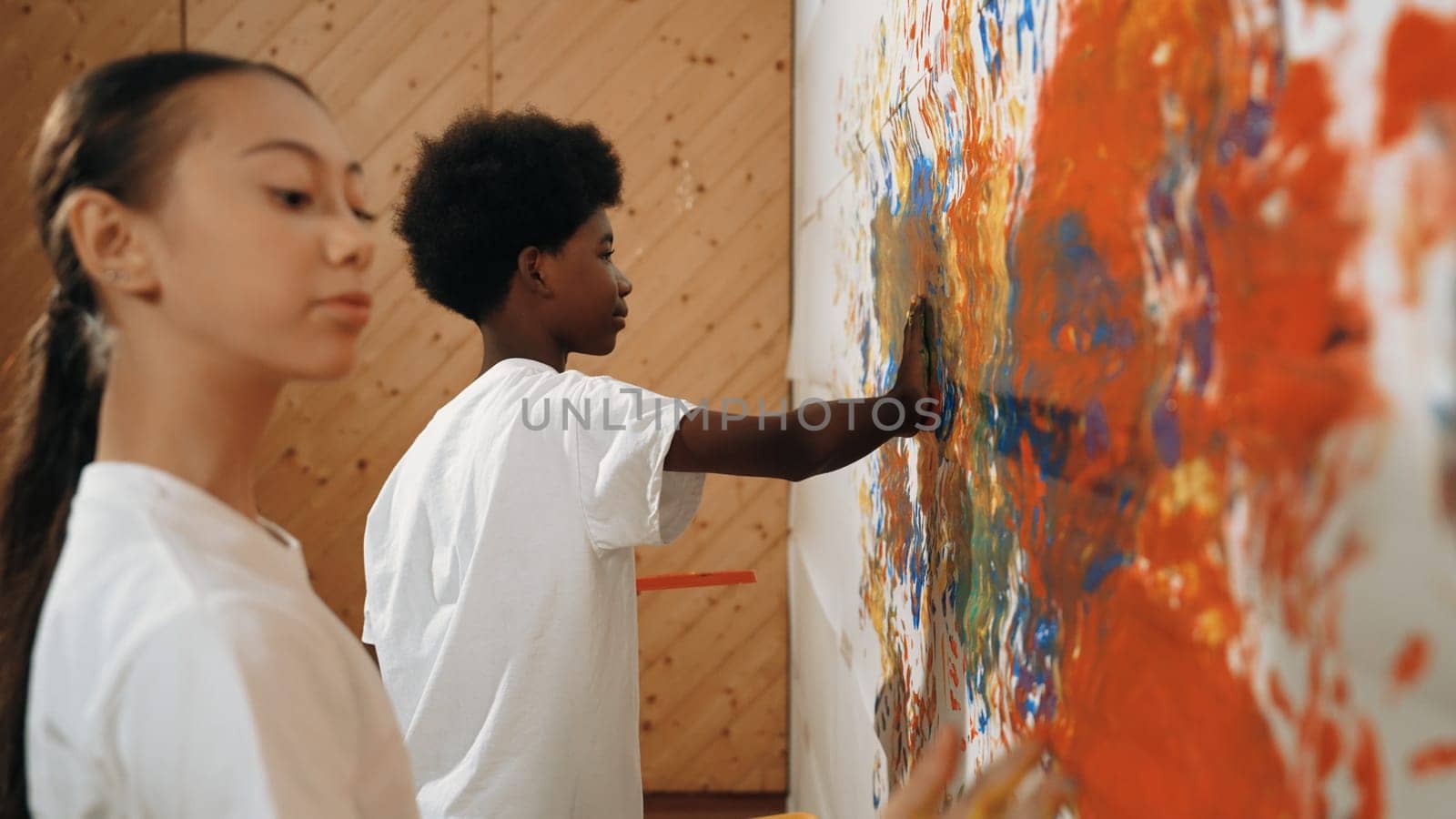 Diverse happy highschool girl and african boy paint the wall with water color in red and blue or contrast color by using their hands in art lesson. Side view. Creative activity concept. Edification.