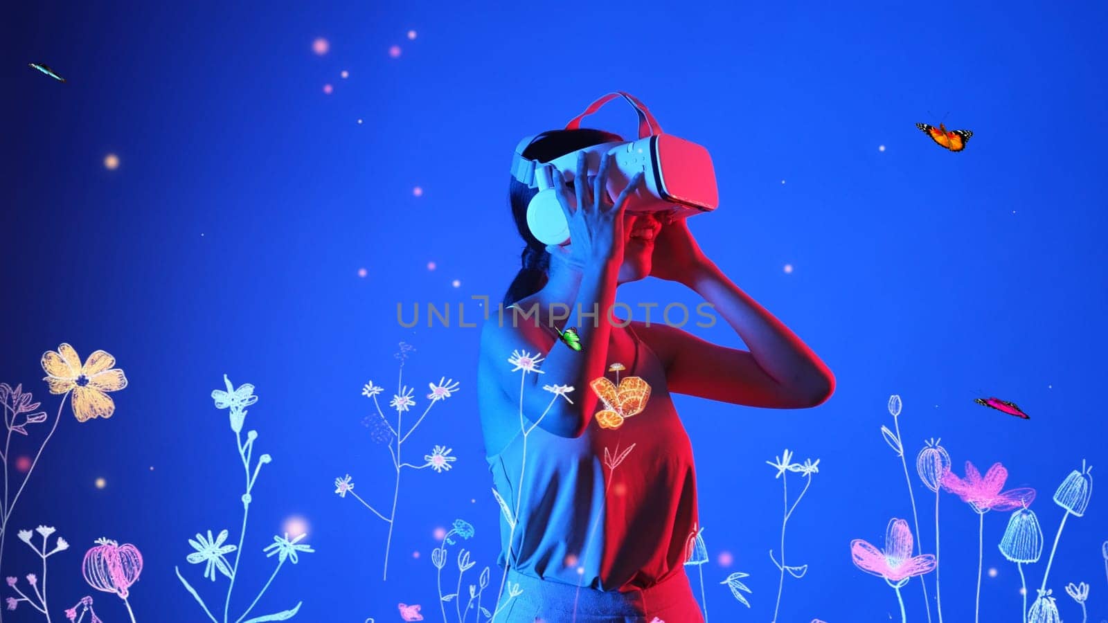 Beautiful Asian woman with VR to metaverse interacting virtual neon flower playing with butterfly flying new neon blossom blue background 3D pollen graphic floating meta garden world. Hallucination.