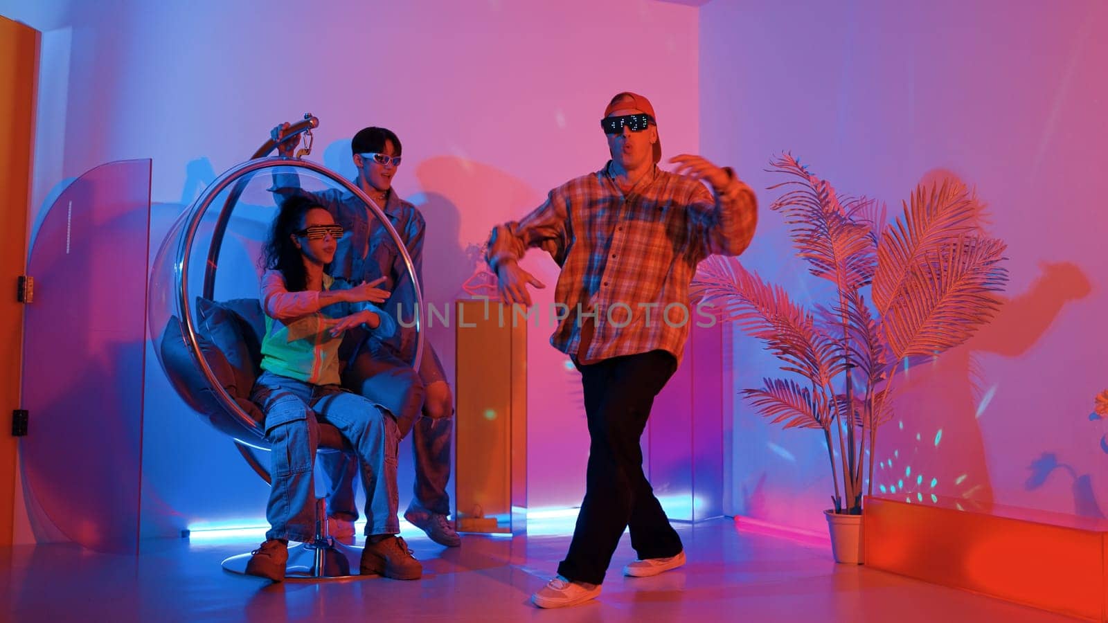 Happy hipster show break dancing while multicultural friend with casual cloth cheering at studio. Professional street dancer perform hip hop beat or lively rhyme with neon or led light. Regalement.