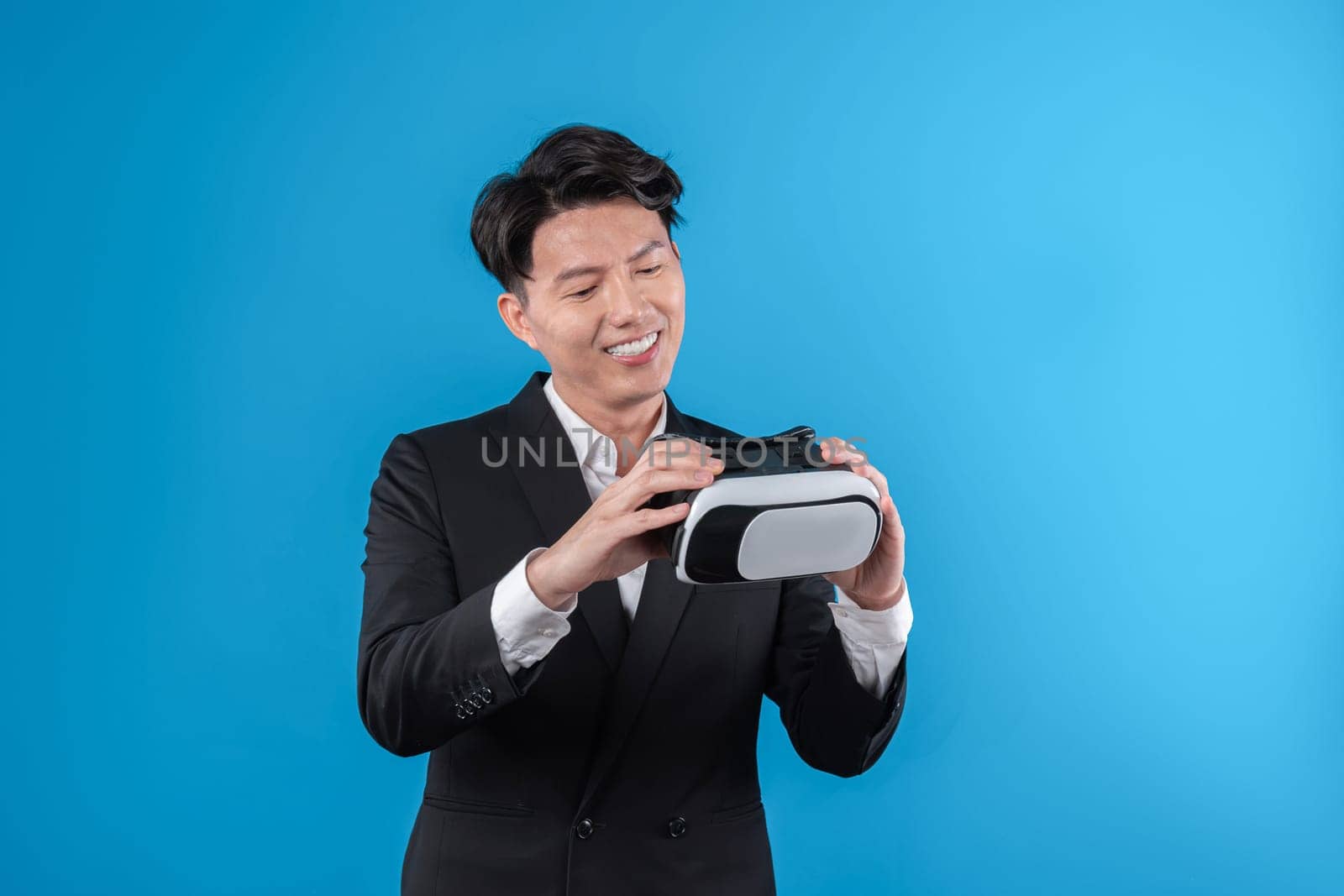 Smiling Asian businessman looking through VR connecting financial business report futuristic metaverse data analytics power bi technology virtual reality meta isolated blue copyspace. Contrivance.