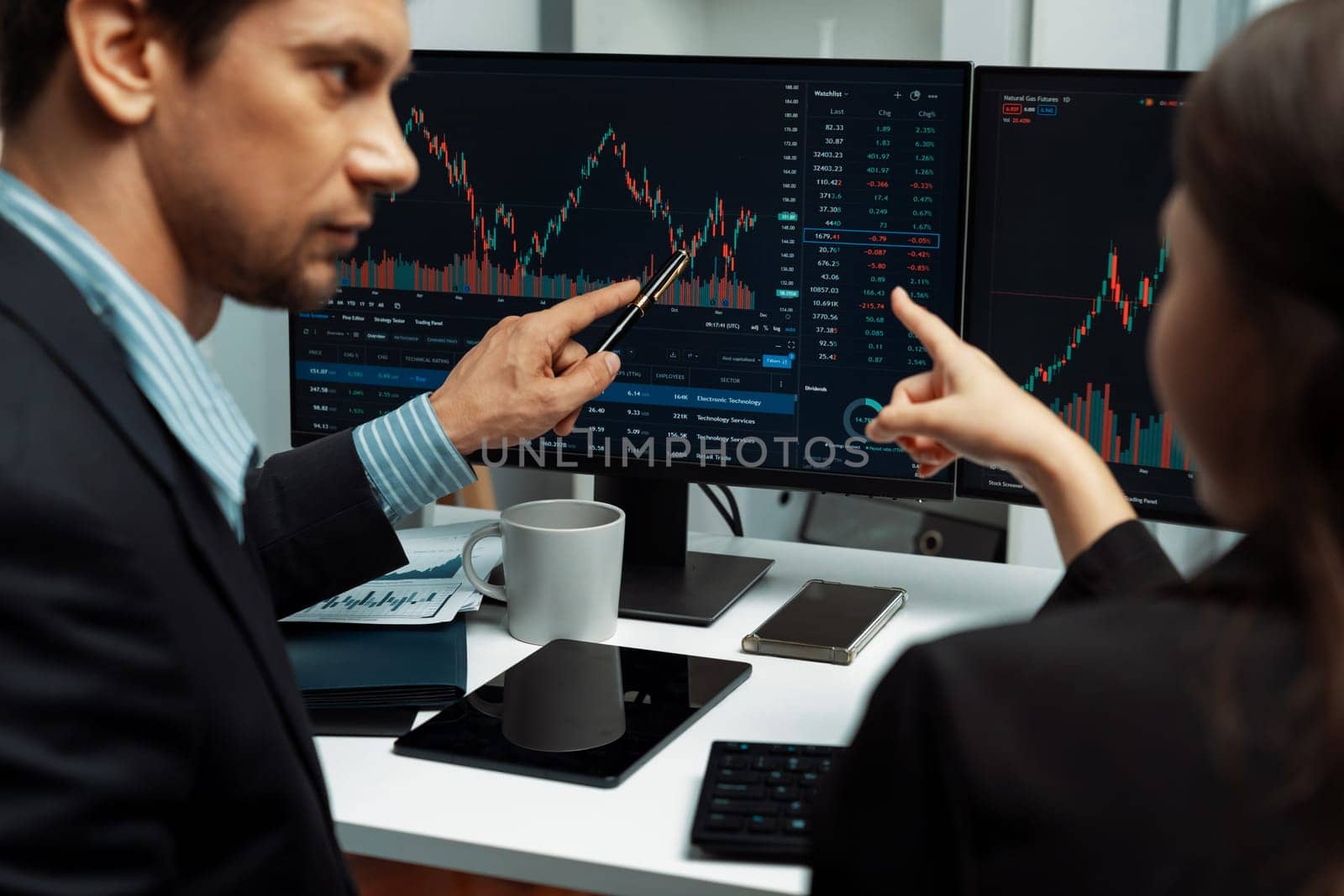 Two business traders discussing on dynamic stock market in currency rate investment trading on two pc screens with compare real time graph on risk or profit point of data at modern office. Postulate.