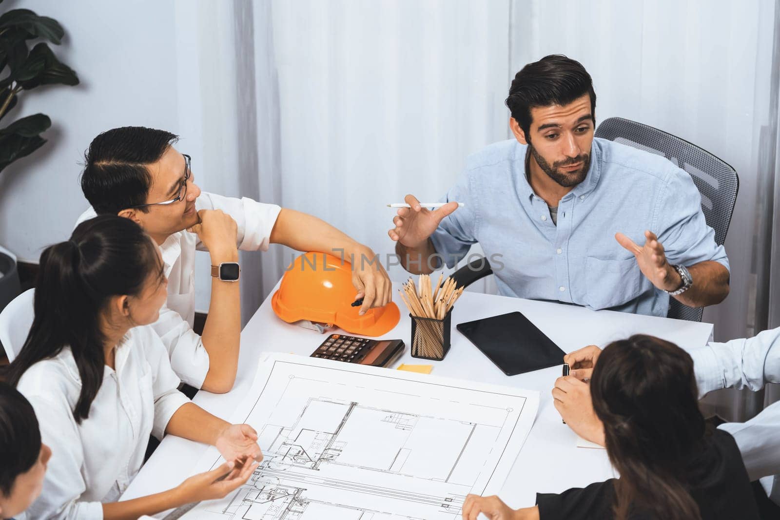 Diverse group of civil engineer and client working together on architectural project, reviewing construction plan and building blueprint at meeting table. Prudent