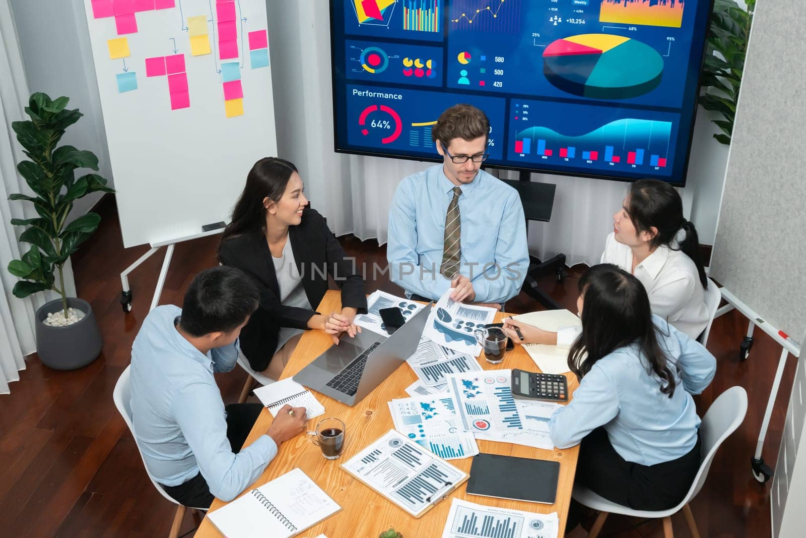 Diverse group of business analyst team analyzing financial data report. Finance data analysis chart and graph dashboard show on TV screen in meeting room for strategic marketing planning. Habiliment