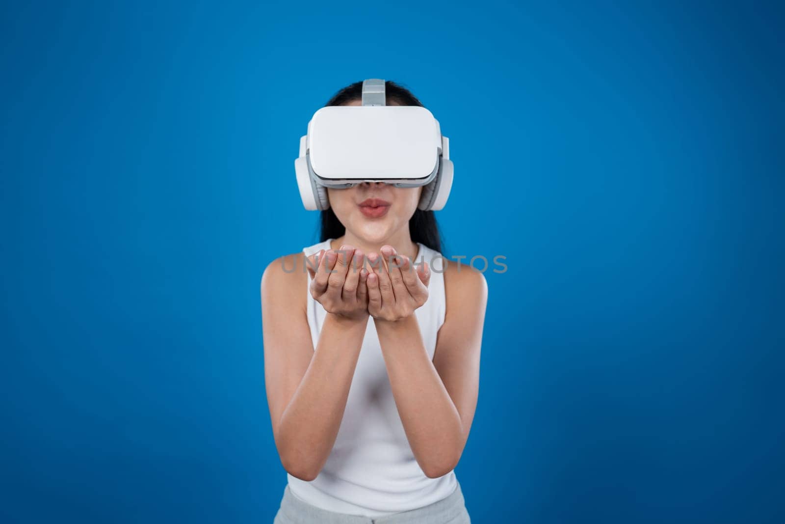 Smart female standing with blue background wearing VR headset connecting metaverse, futuristic cyberspace community technology. Elegant woman excited seeing generated virtual scenery. Hallucination.