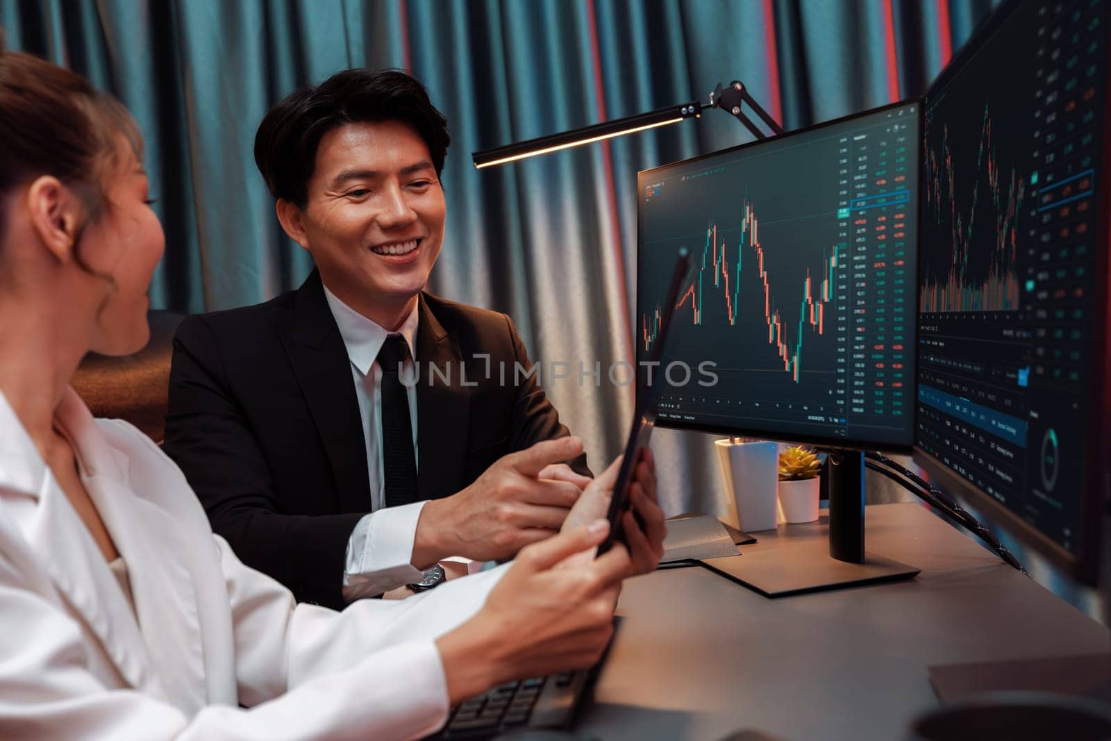 Businesswoman holding tablet on dynamic stock exchange statistic online showing to partners to share, comparing with high or low point graph on computer screen at night neon modern office. Infobahn.