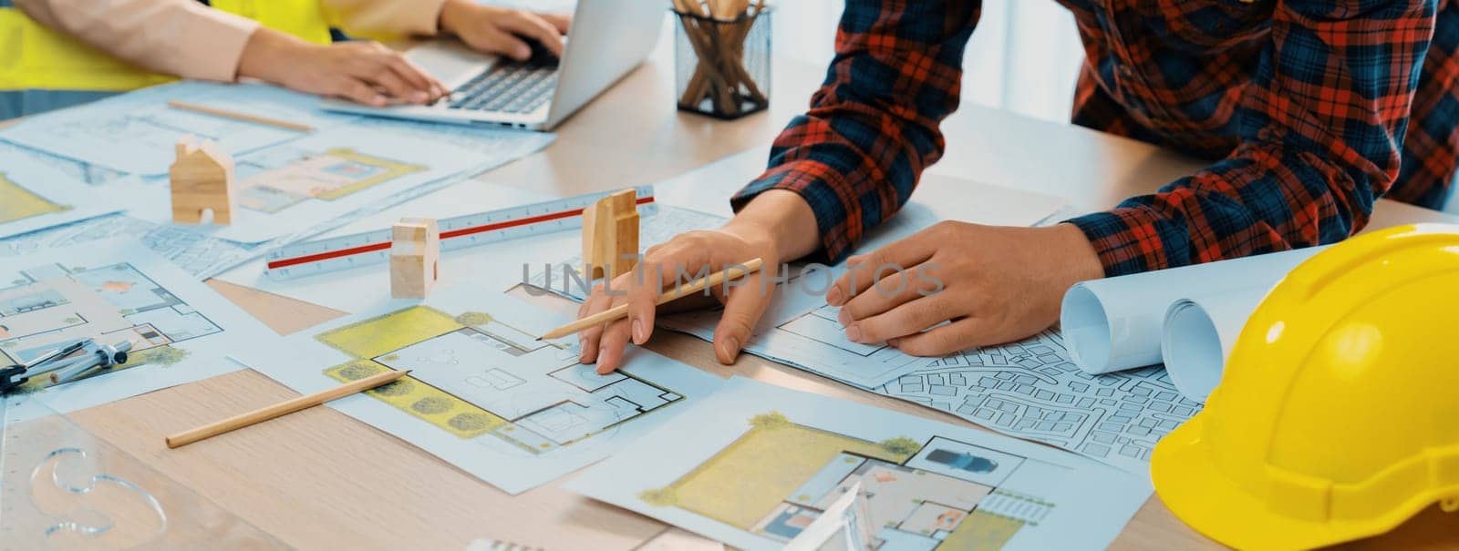 A cropped portrait of professional architect working with blueprint during safety engineer using laptop analysis data at meeting table with document scatter around. Close up. Delineation.